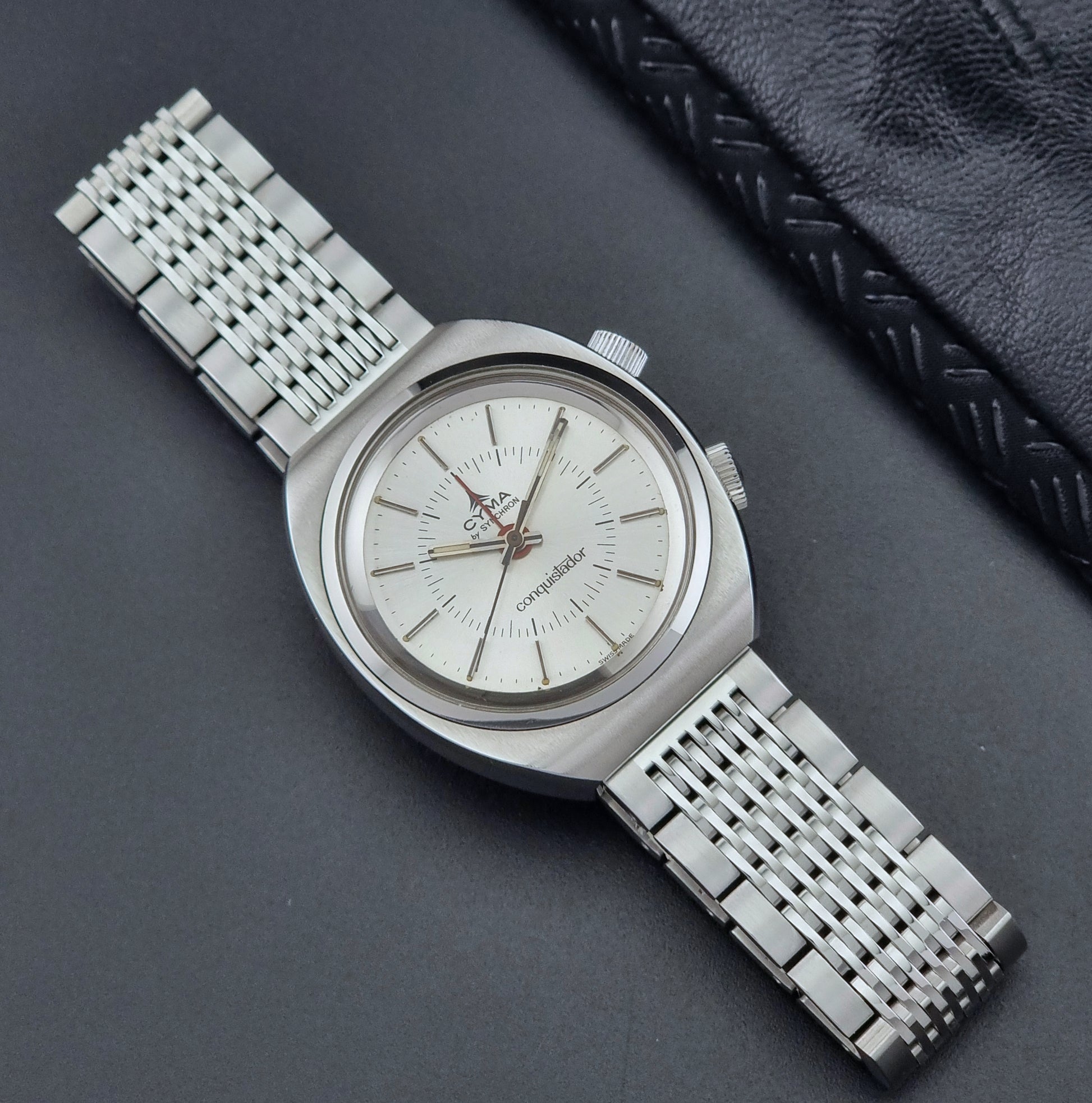 Vintage Cyma Alarm watch by Synchron a Conquistador 34270 with a detailed face on a dark surface front