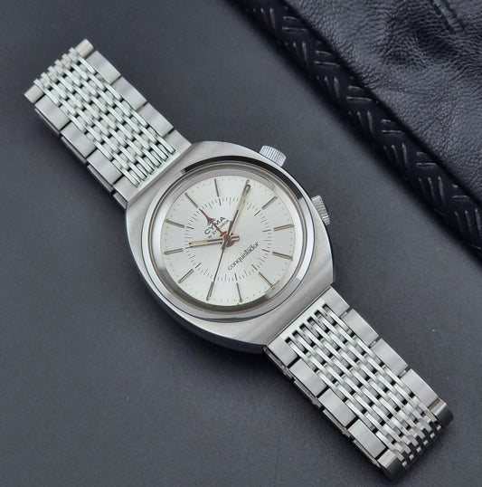 Vintage Cyma Alarm watch by Synchron a Conquistador 34270 with a detailed face on a dark surface front
