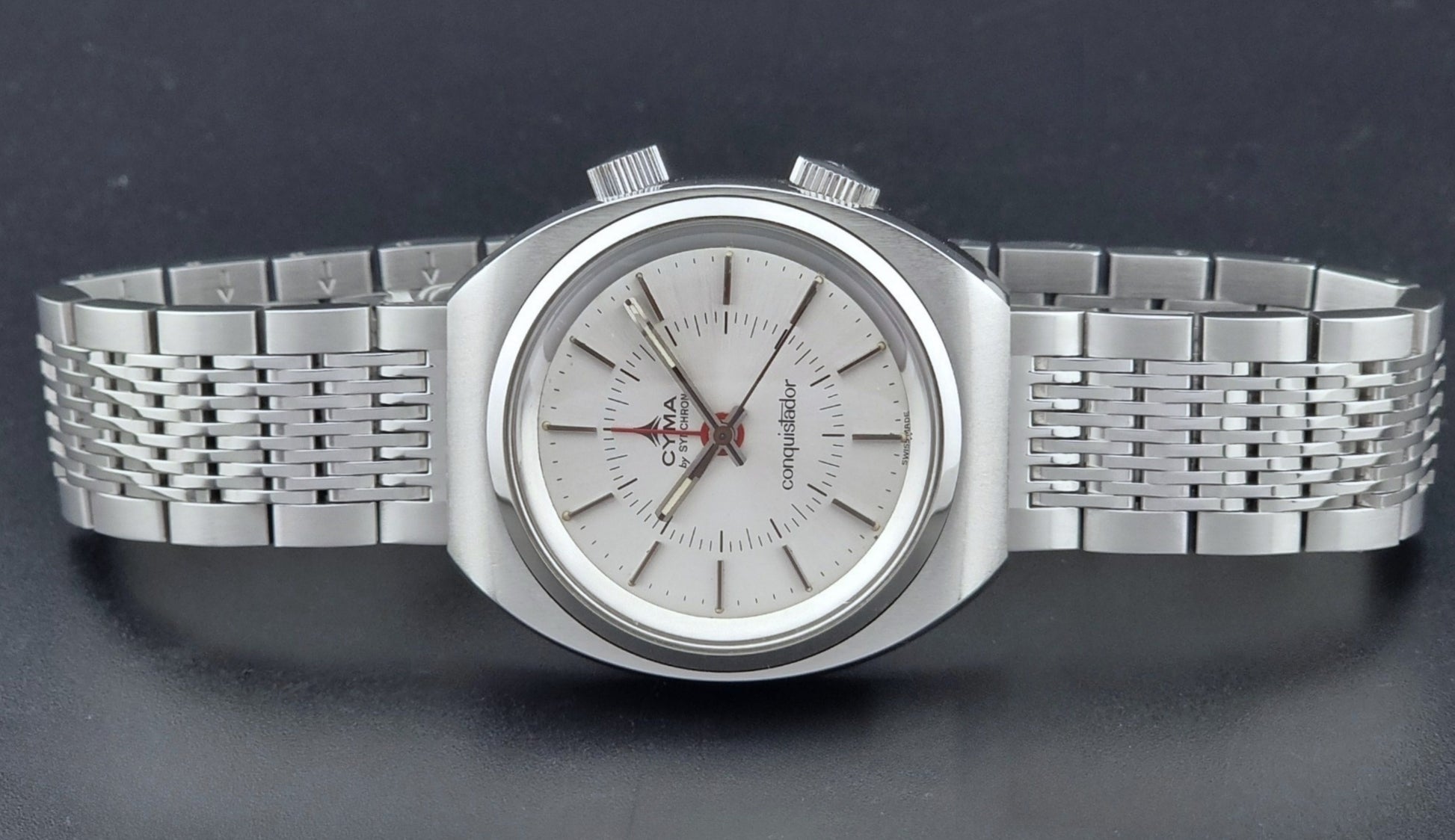 Vintage Cyma Alarm watch by Synchron a Conquistador 34270 with a detailed face on a dark surface dial view