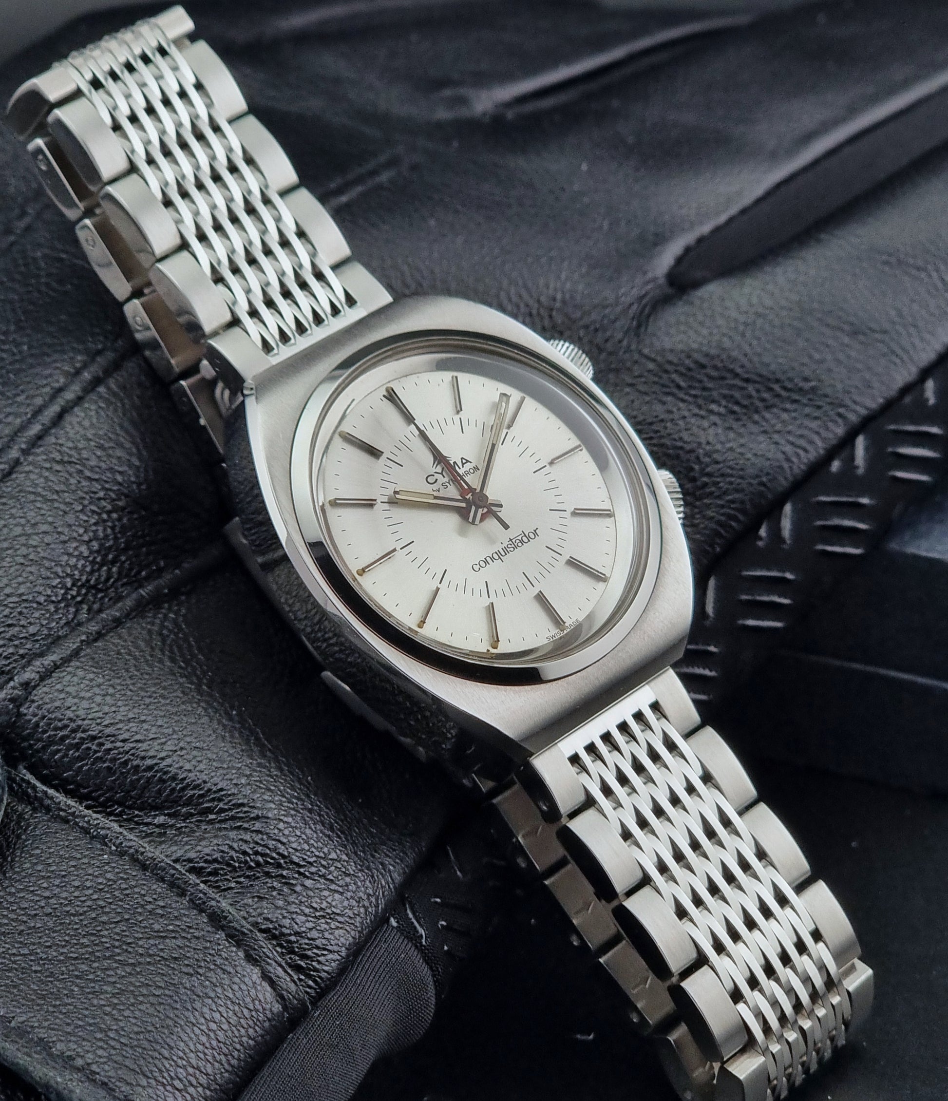 Vintage Cyma Alarm watch by Synchron a Conquistador 34270 with a detailed face on a dark surface side view