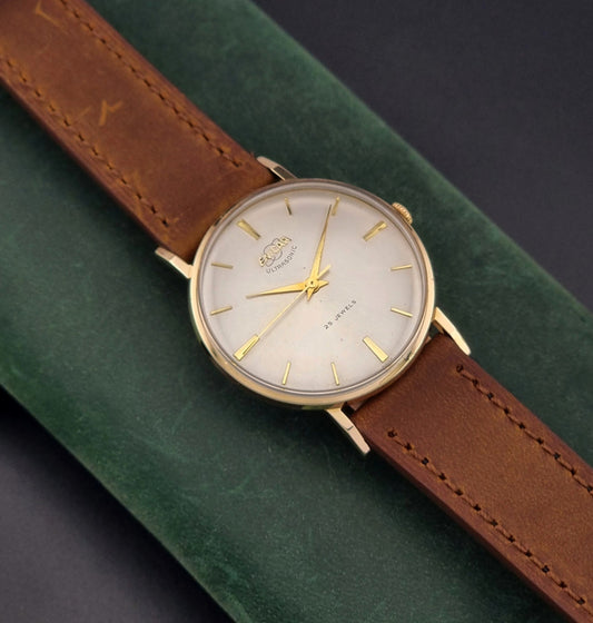 Vintage Enicar Wristwatch Ultrasonic 100/178 with brown leather strap and gold casing on a green surface front