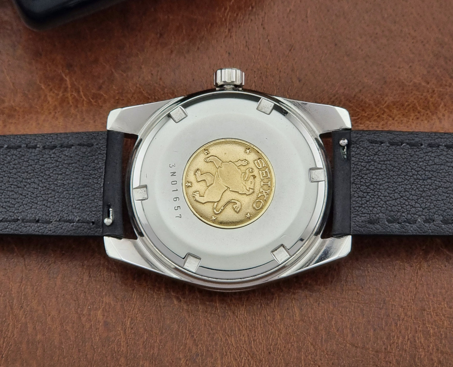 Vintage Grand Seiko Wristwatch with black leather strap on a brown background case back view