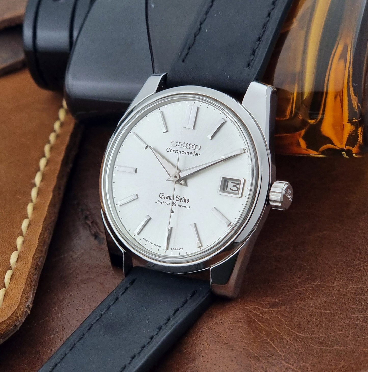 Vintage Grand Seiko Wristwatch with black leather strap on a brown background crown view