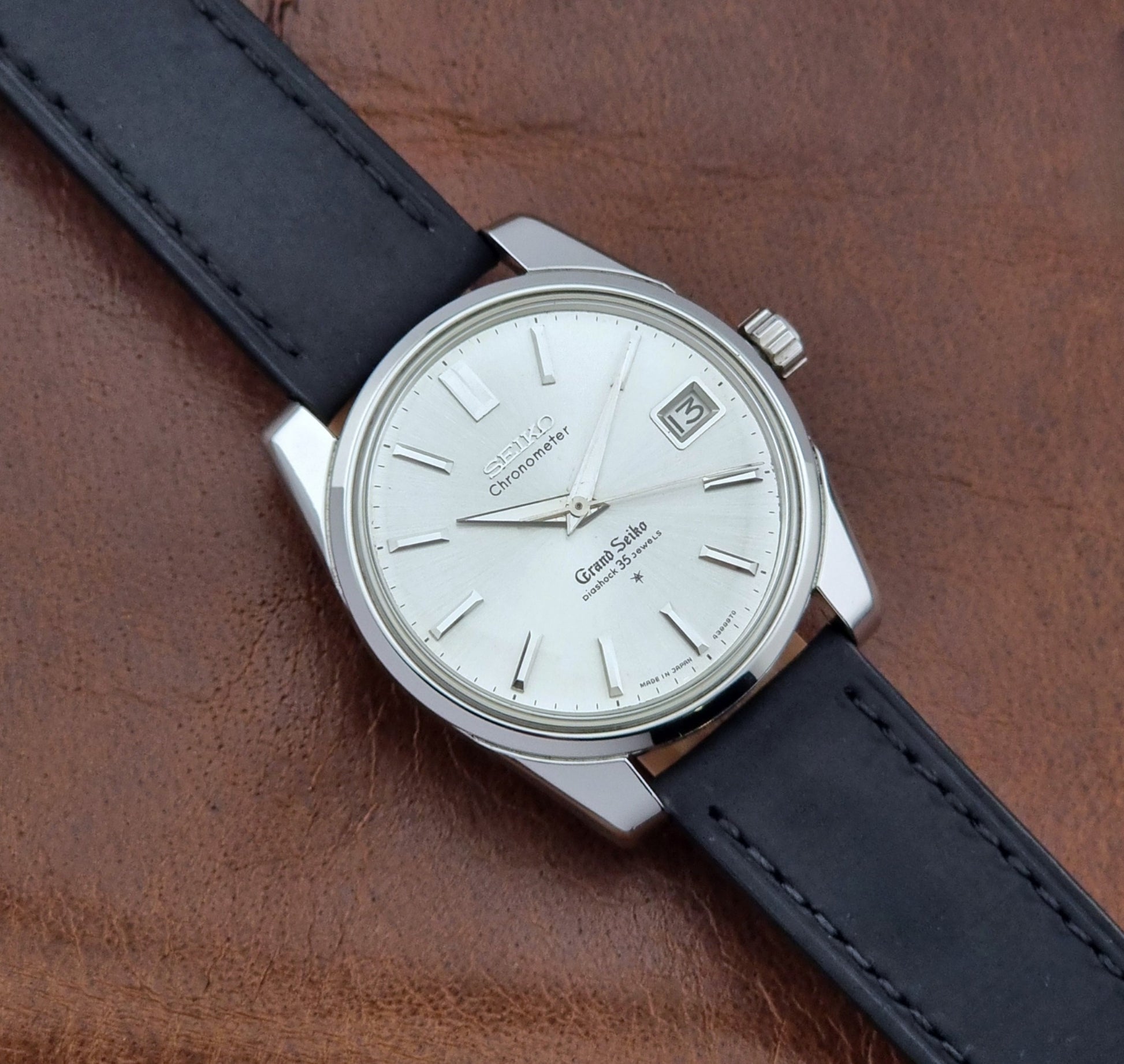 Vintage Grand Seiko Wristwatch with black leather strap on a brown background front view