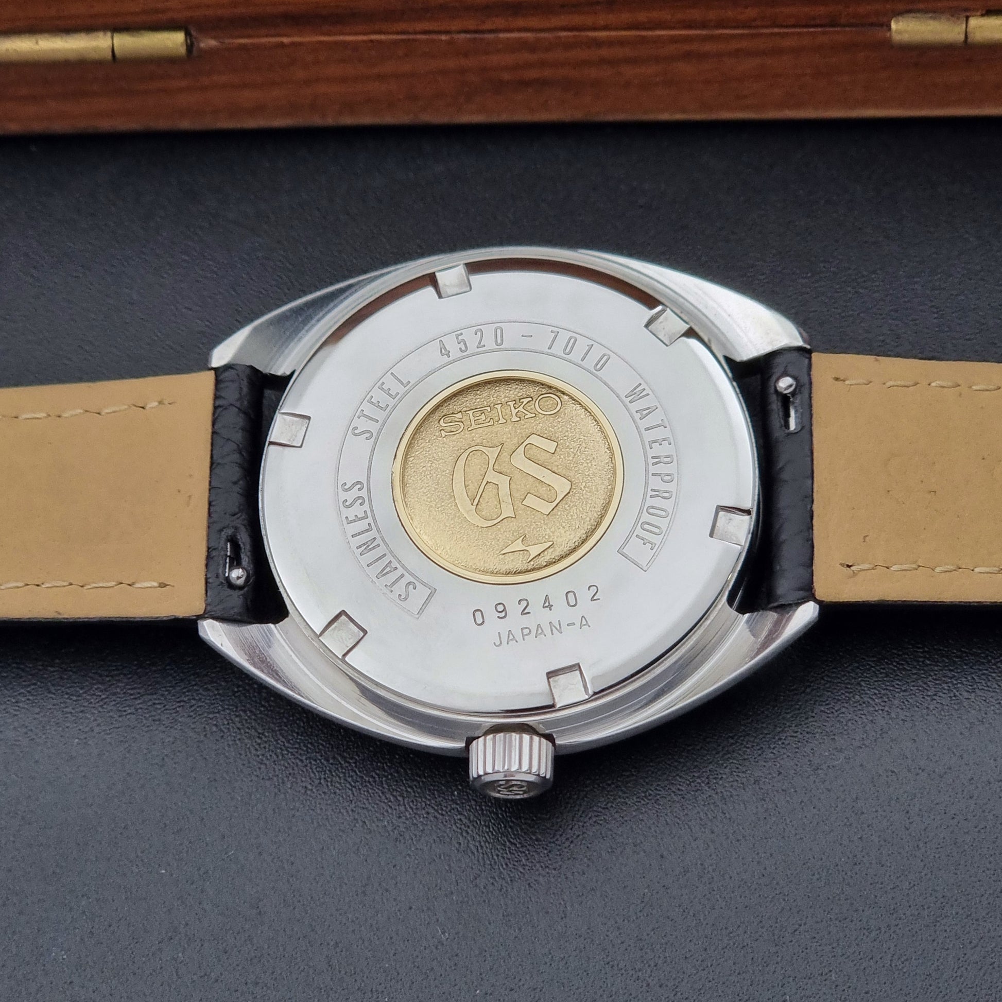 Grand Seiko watch 4520-7010 close up of its case back showing the GS gold medallion with black leather strap  on a  on a dark surface 