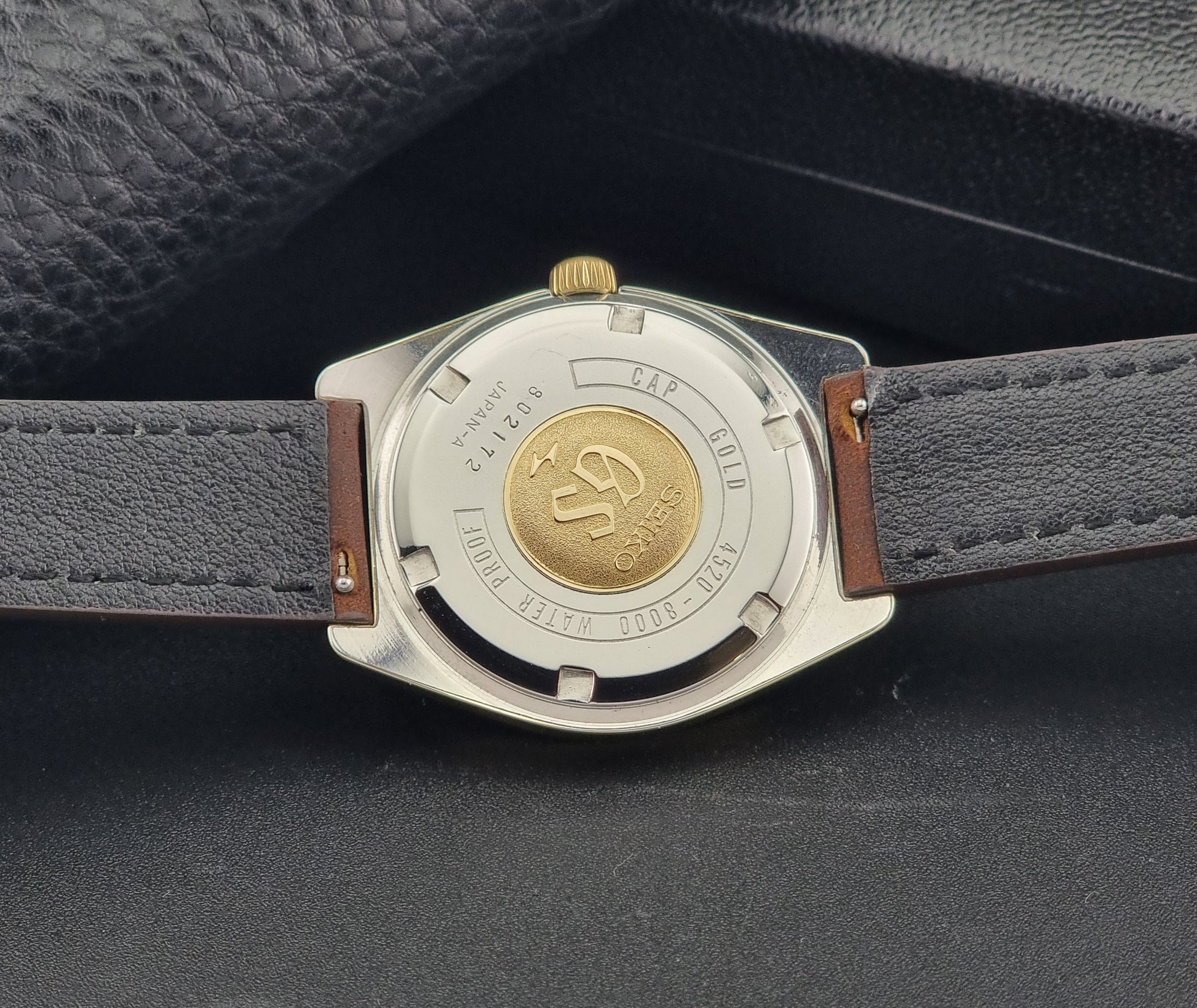 Vintage Grand Seiko Gold 4520-8000 wristwatch with a brown leather strap on a dark textured background case back