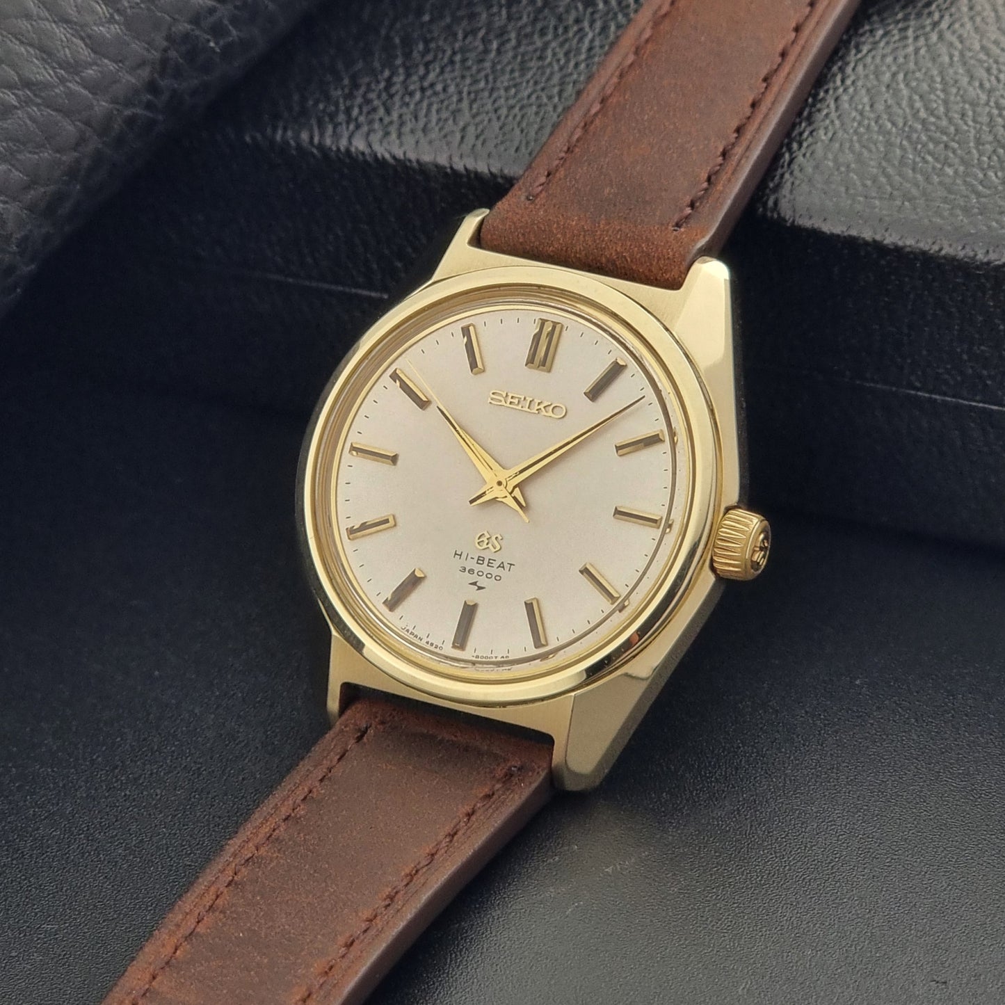 Vintage Grand Seiko Gold 4520-8000 wristwatch with a brown leather strap on a dark textured background crown