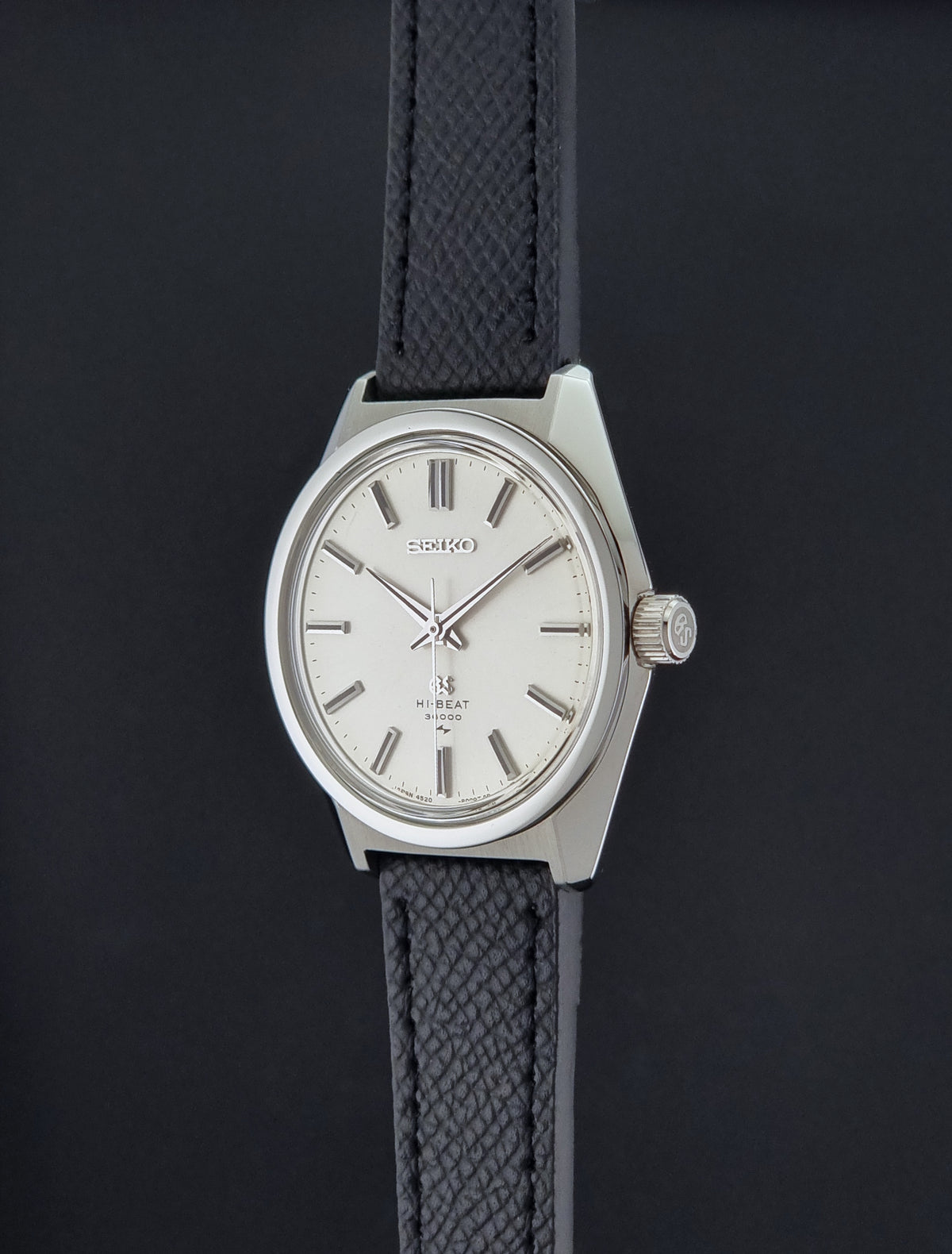 A vintage Grand Seiko watch 4520-8000 with a stainless steel case and black leather strap looking at the crown side, suspended on a dark background