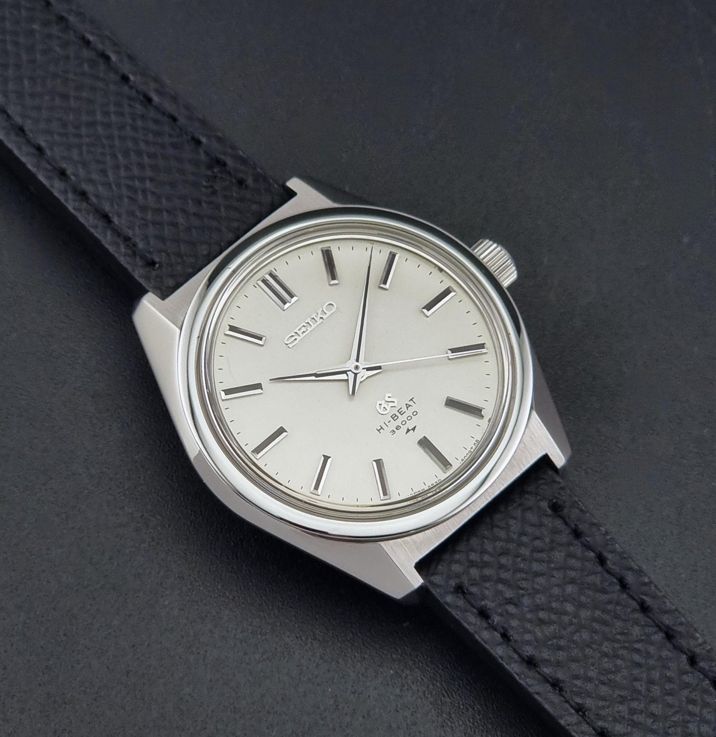 A vintage Grand Seiko watch 4520-8000 with a stainless steel case and black leather strap on a dark background close up view of the sunburst dial
