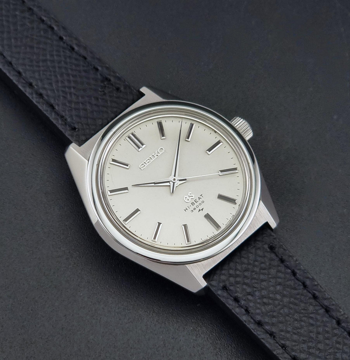 A vintage Grand Seiko watch 4520-8000 with a stainless steel case and black leather strap on a dark background close up view of the sunburst dial