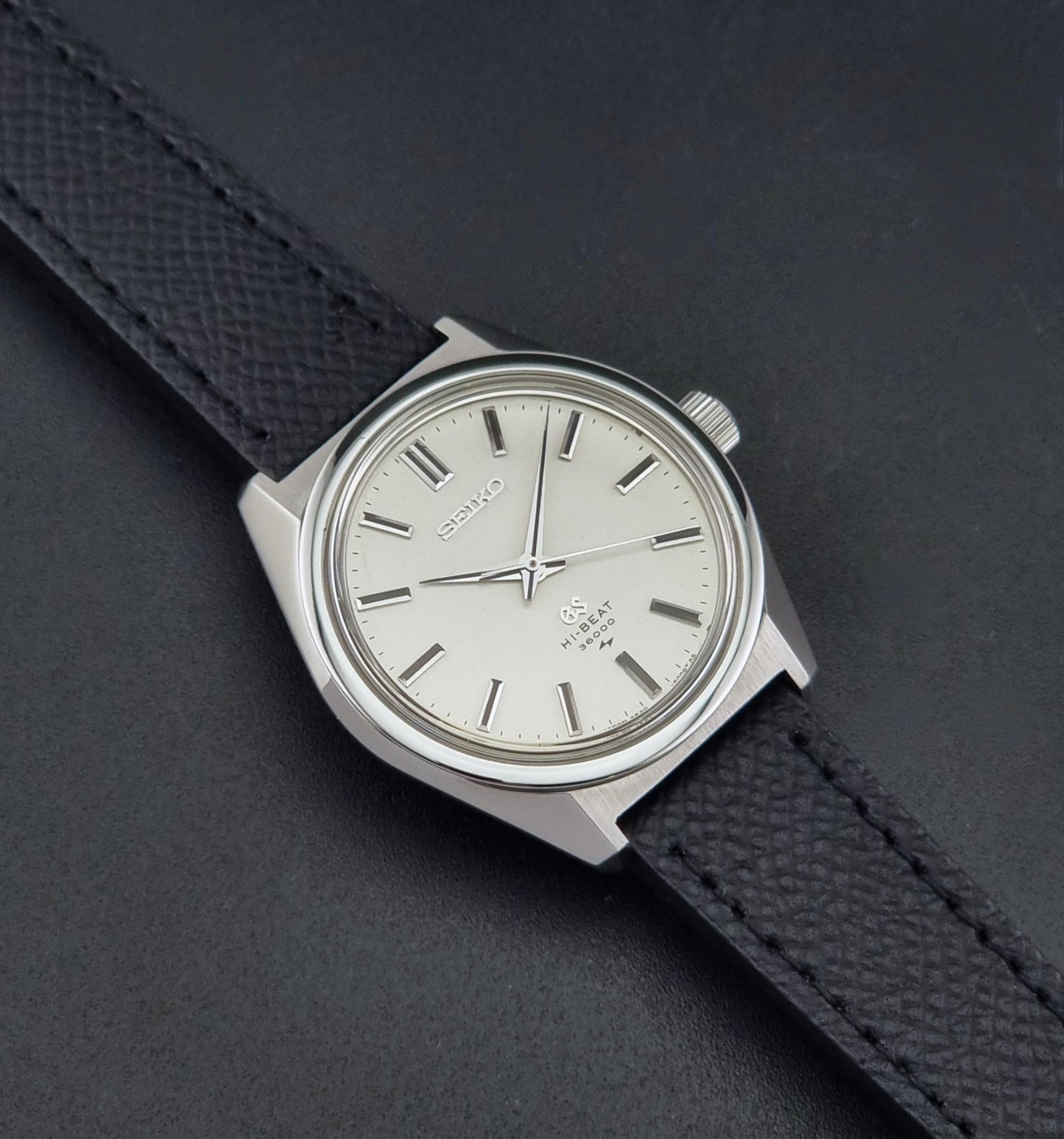 A vintage Grand Seiko watch 4520-8000 with a stainless steel case and black leather strap on a dark background