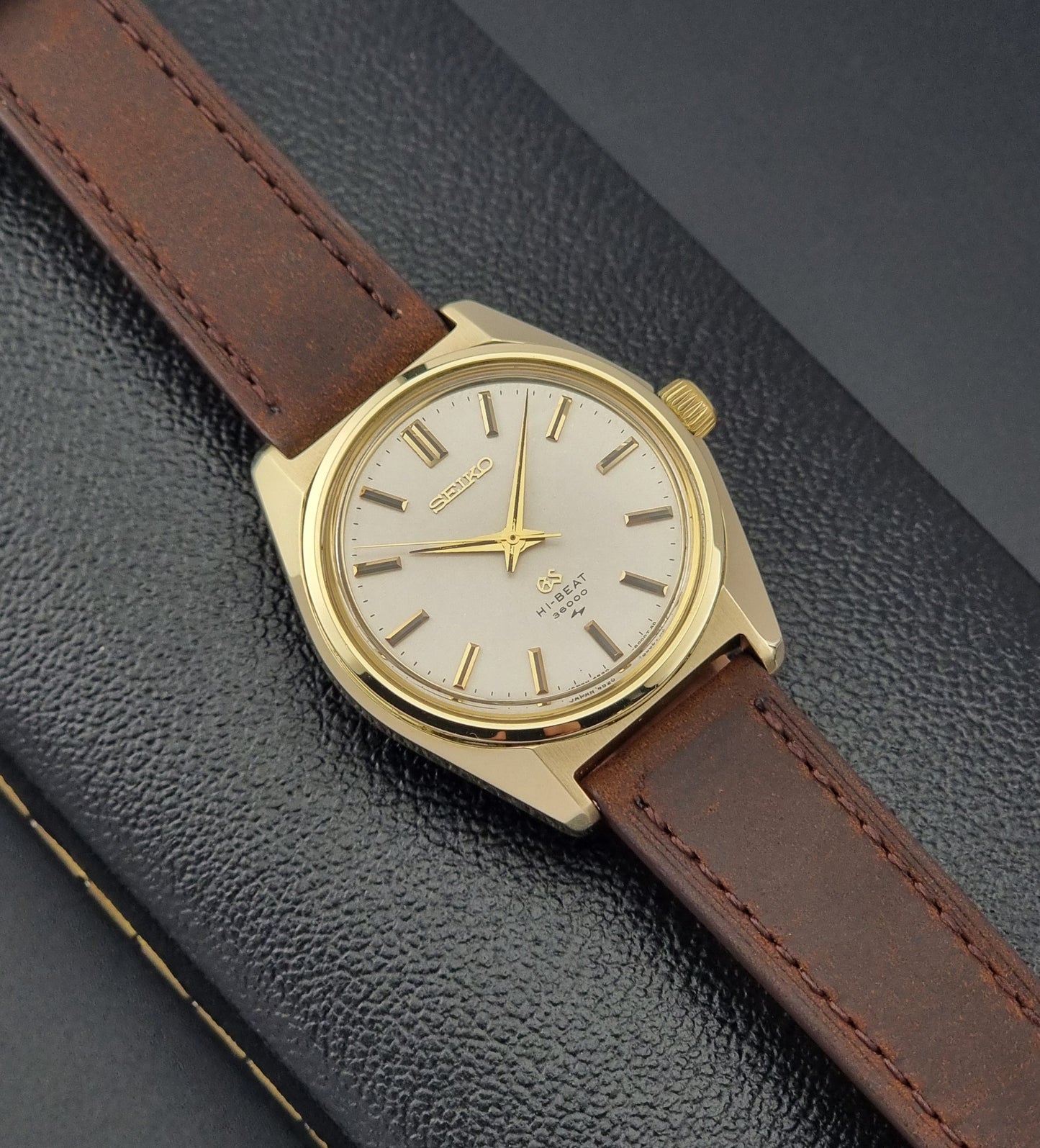 Vintage Grand Seiko Gold 4520-8000 wristwatch with a brown leather strap on a dark textured background