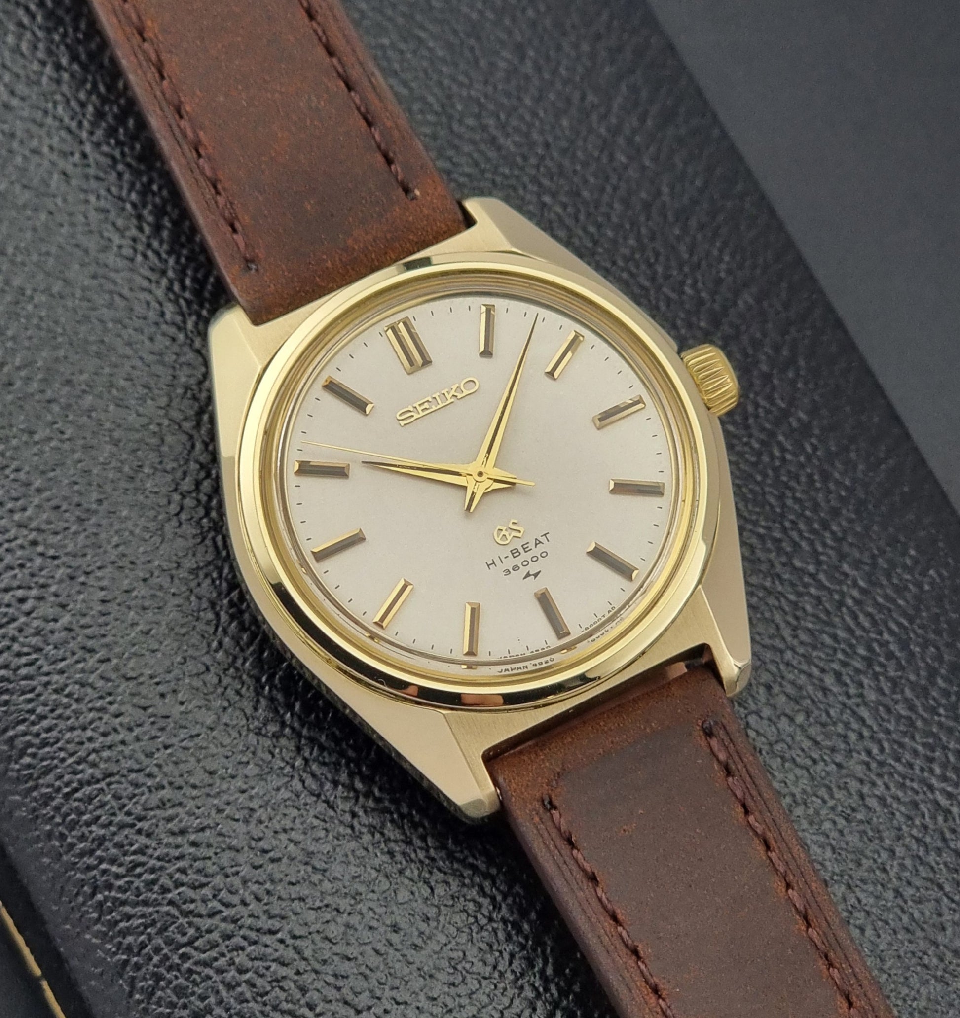 Vintage Grand Seiko Gold 4520-8000 wristwatch with a brown leather strap on a dark textured background close front view