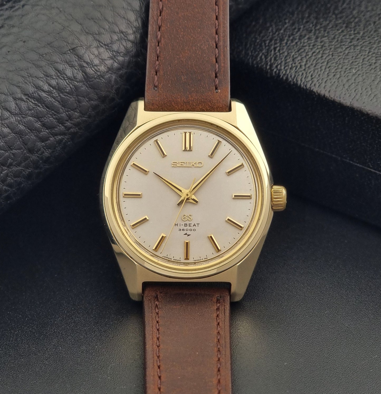 Vintage Grand Seiko Gold 4520-8000 wristwatch with a brown leather strap on a dark textured background front