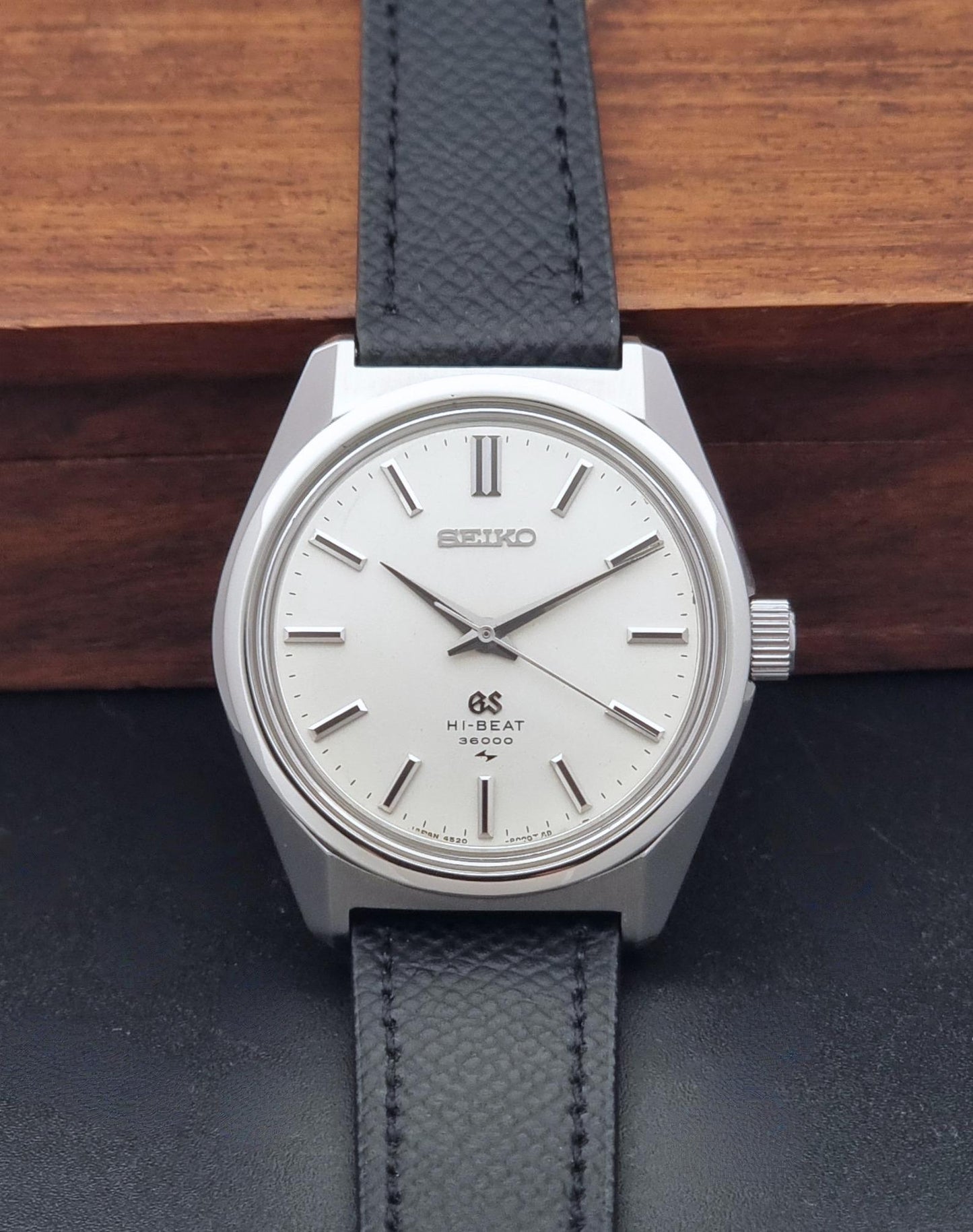 A vintage Grand Seiko watch 4520-8000 with a stainless steel case and black leather strap on a dark background view of the dial