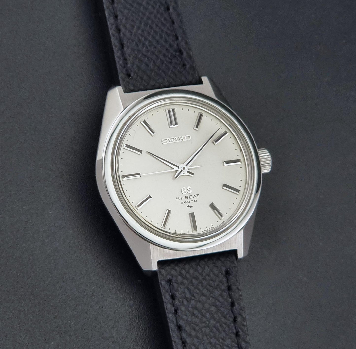 A vintage Grand Seiko watch 4520-8000 with a stainless steel case and black leather strap close up view on the sunburst dial on a dark background