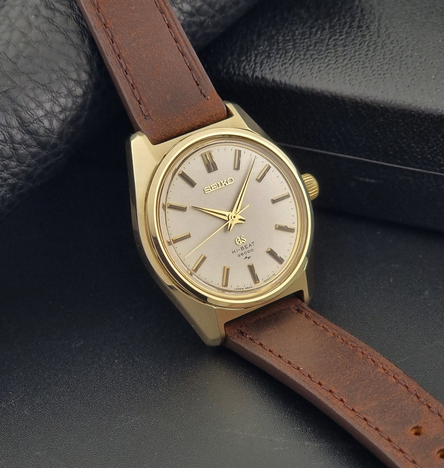 Vintage Grand Seiko Gold 4520-8000 wristwatch with a brown leather strap on a dark textured background side