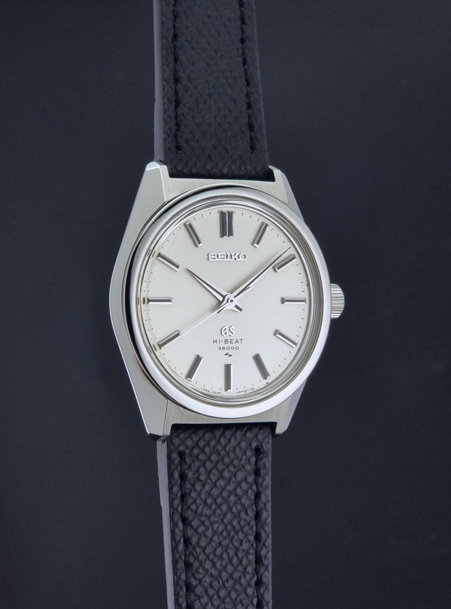 A vintage Grand Seiko watch 4520-8000 with a stainless steel case and black leather strap suspended on a dark background