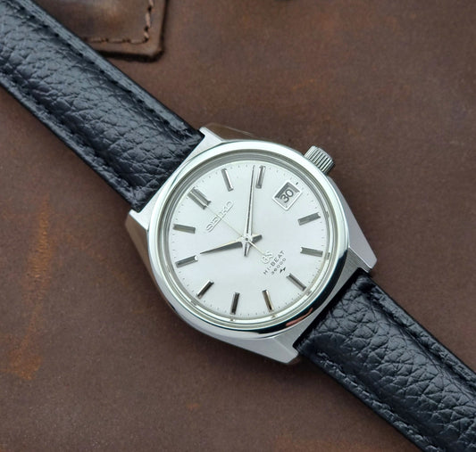 Vintage Grand Seiko watch with black leather strap on a brown leather background