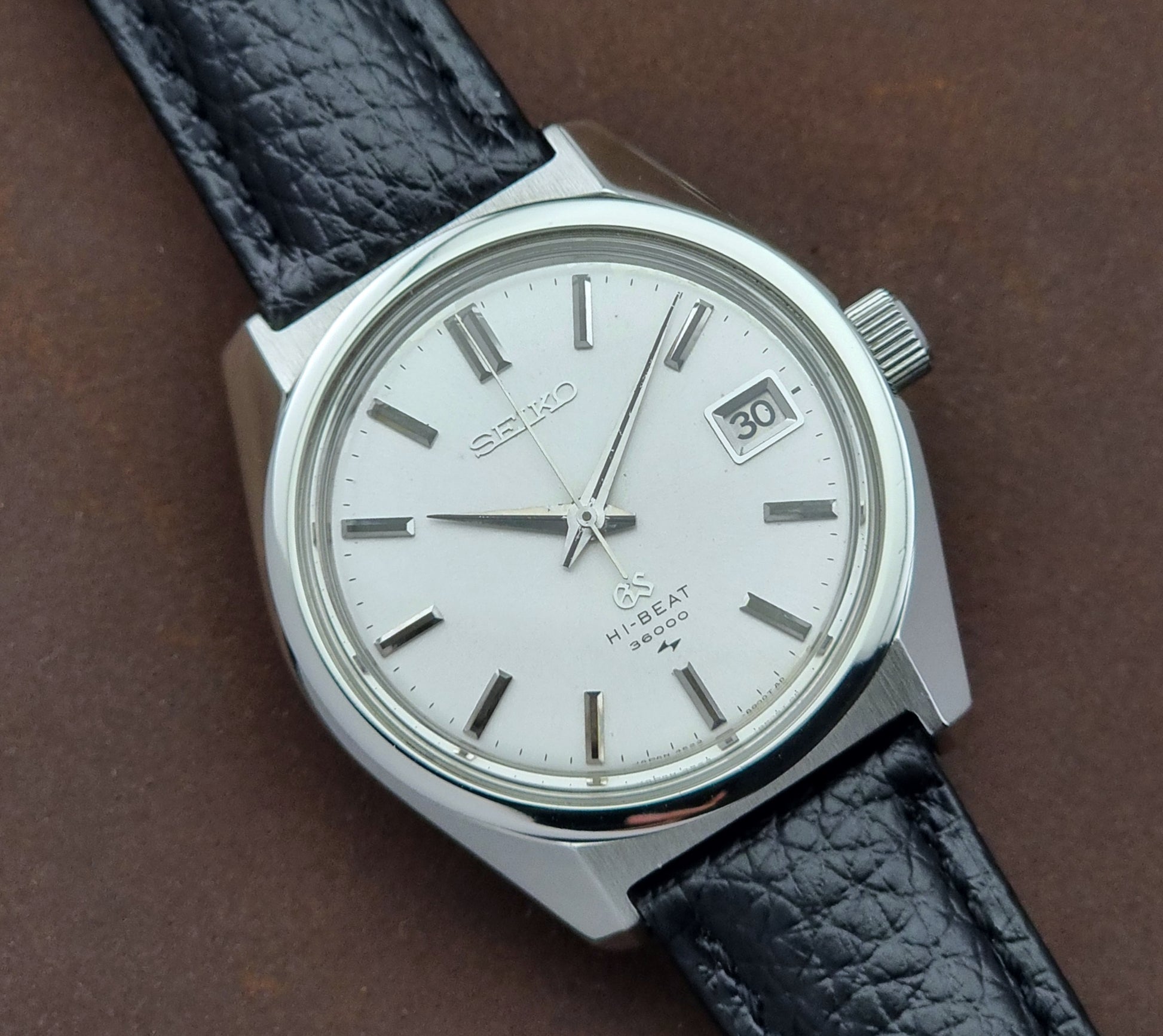 Vintage Grand Seiko watch with black leather strap on a brown background