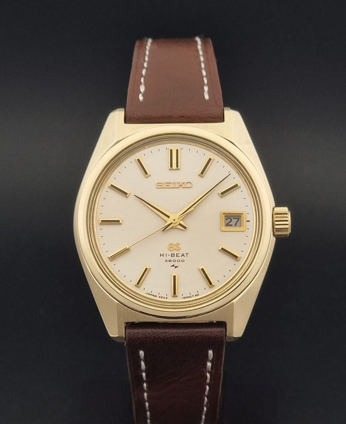 Vintage Grand Seiko watch 4522-8000 with a gold-tone case, cream dial, and brown leather strap with white stitching, shown against a dark background.