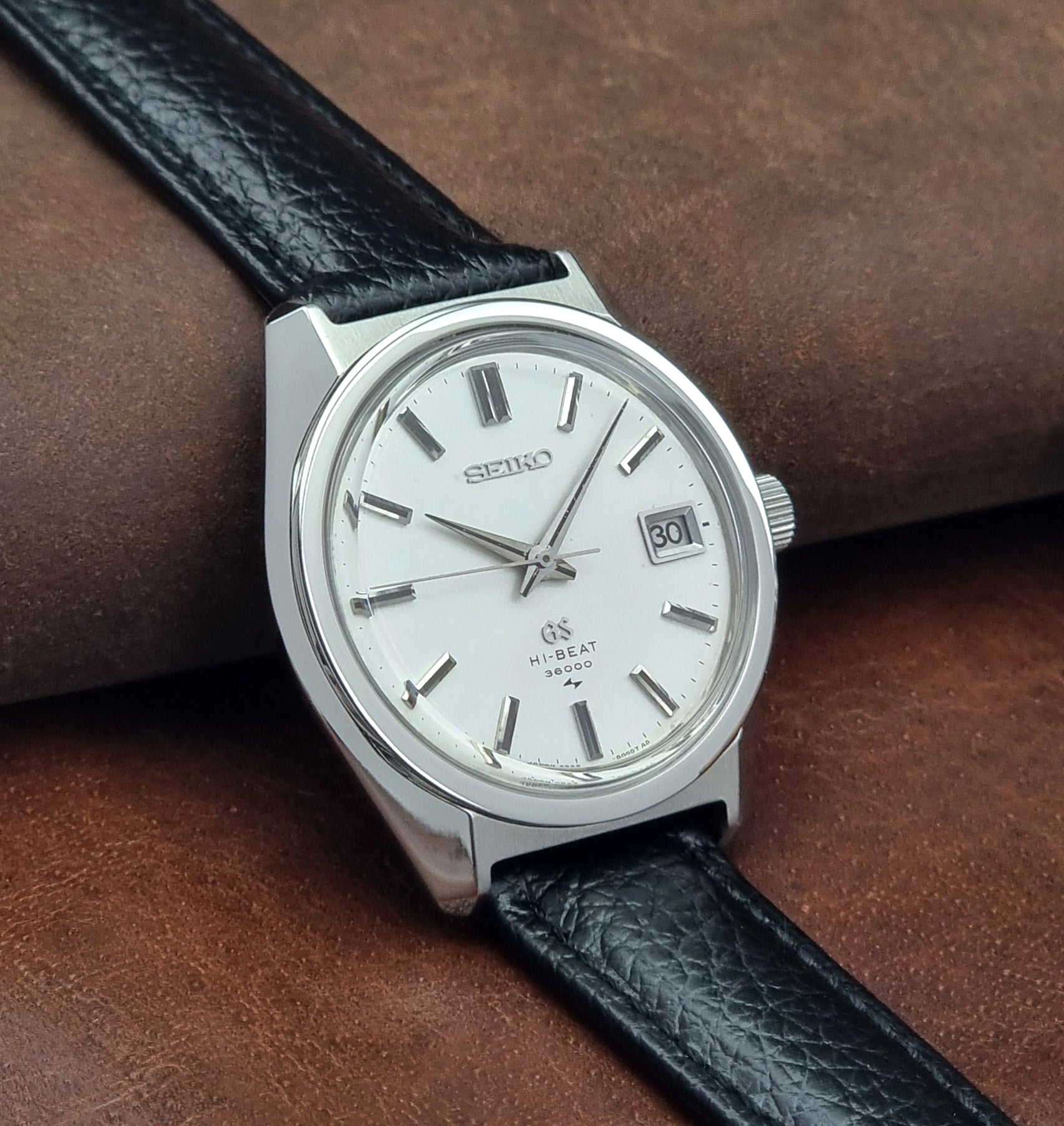Vintage Grand Seiko watch with black leather strap on a brown leather surface