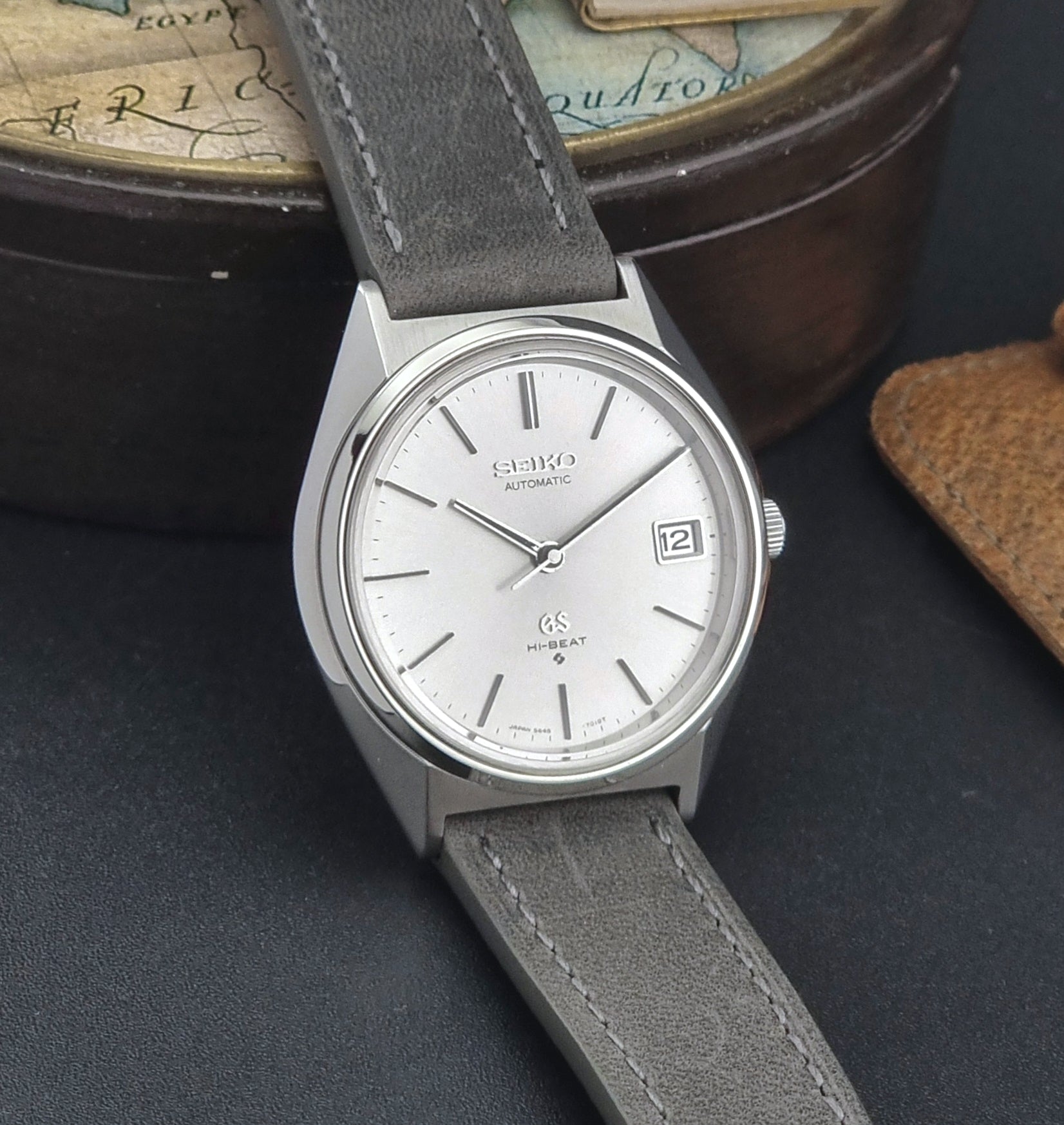 Vintage  Grand Seiko watch with gray strap on a dark surface with a world map in the background