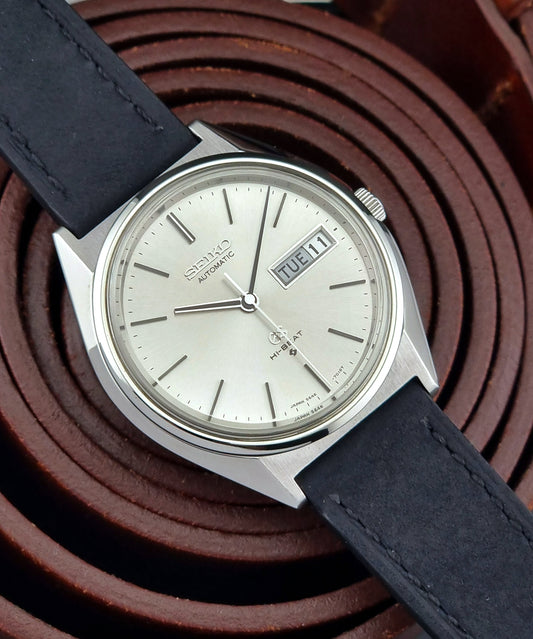 Vintage Grand Seiko watch with black leather strap on a brown textured background