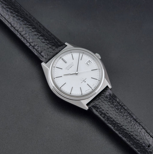 Vintage Grand Seiko Wristwatch 5645-7010 with a silver-toned round case, white dial, and black textured leather strap, on a dark gray background dial