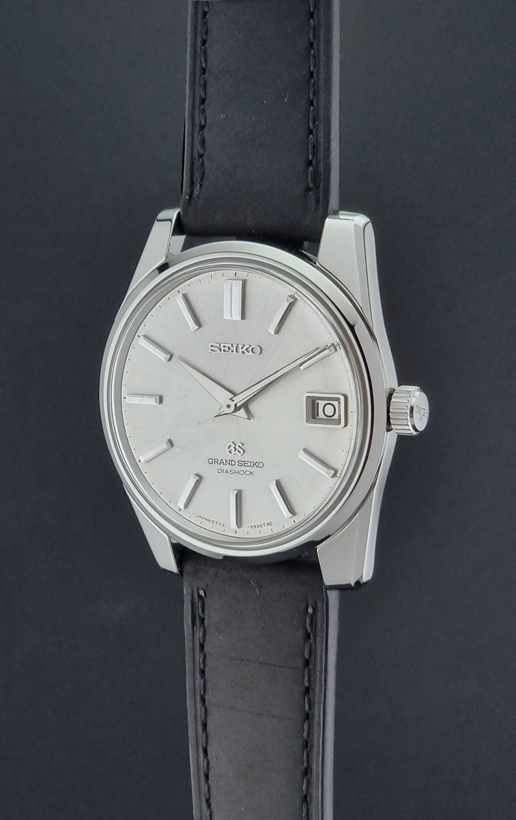 Vintage Grand Seiko Wristwatch 5722-9991 with black leather strap on a gray background crown side profile