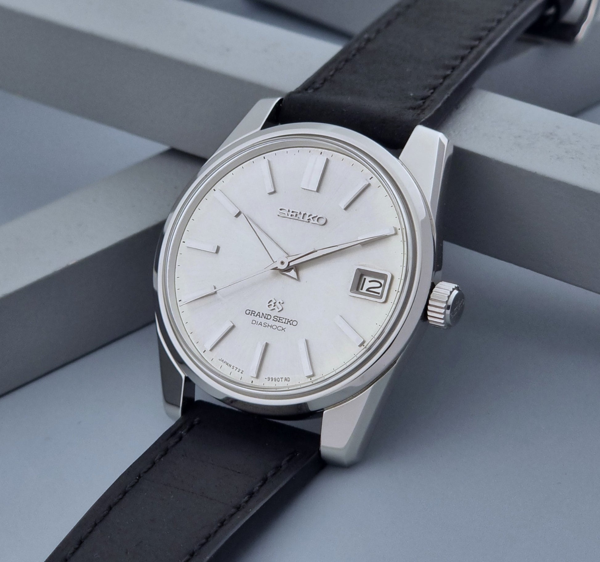 Vintage Grand Seiko Wristwatch 5722-9991 with black leather strap on a gray background crown side