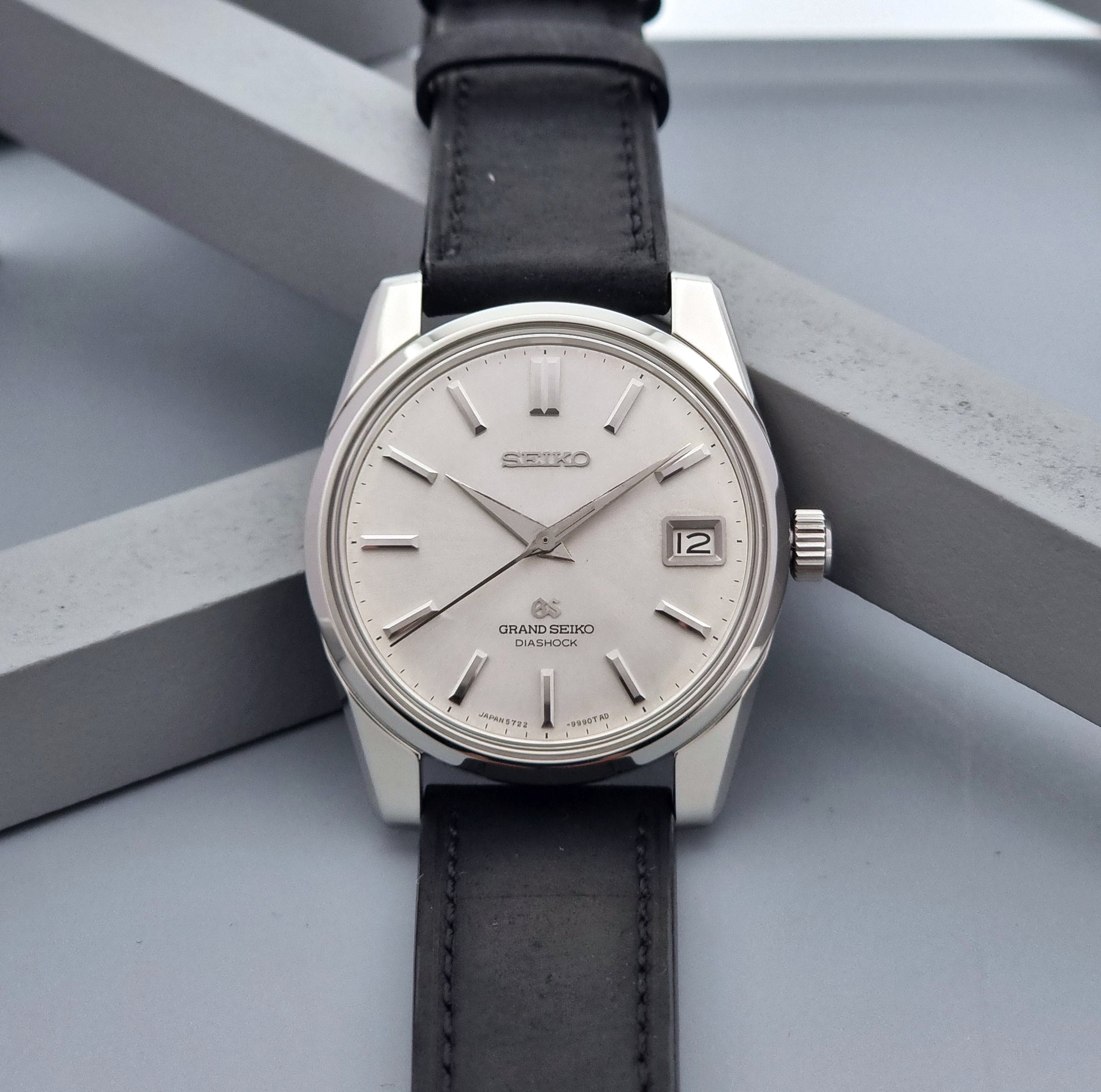 Vintage Grand Seiko Wristwatch 5722-9991 with black leather strap on a gray background front