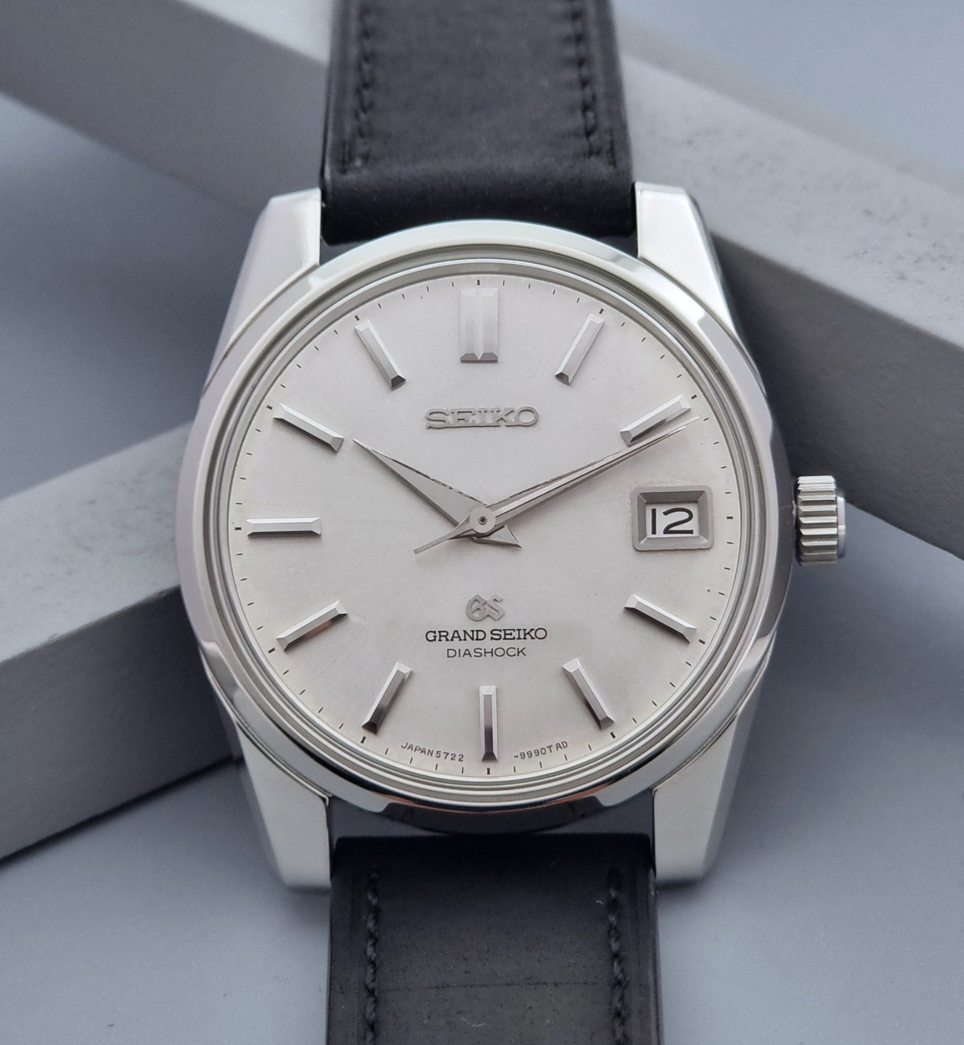 Vintage Grand Seiko Wristwatch 5722-9991 with black leather strap on a gray background dial close up