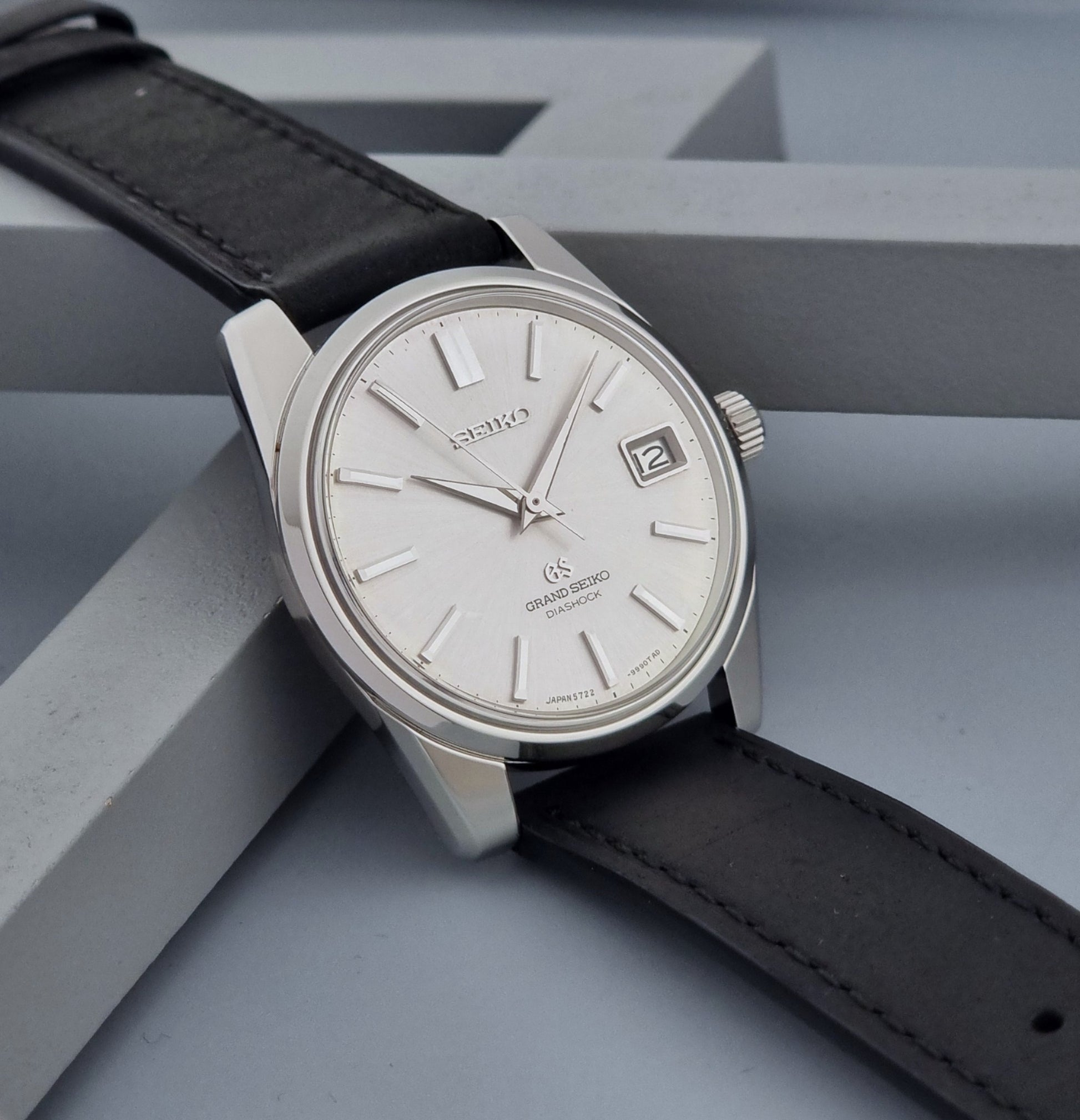 Vintage Grand Seiko Wristwatch 5722-9991 with black leather strap on a gray background side view