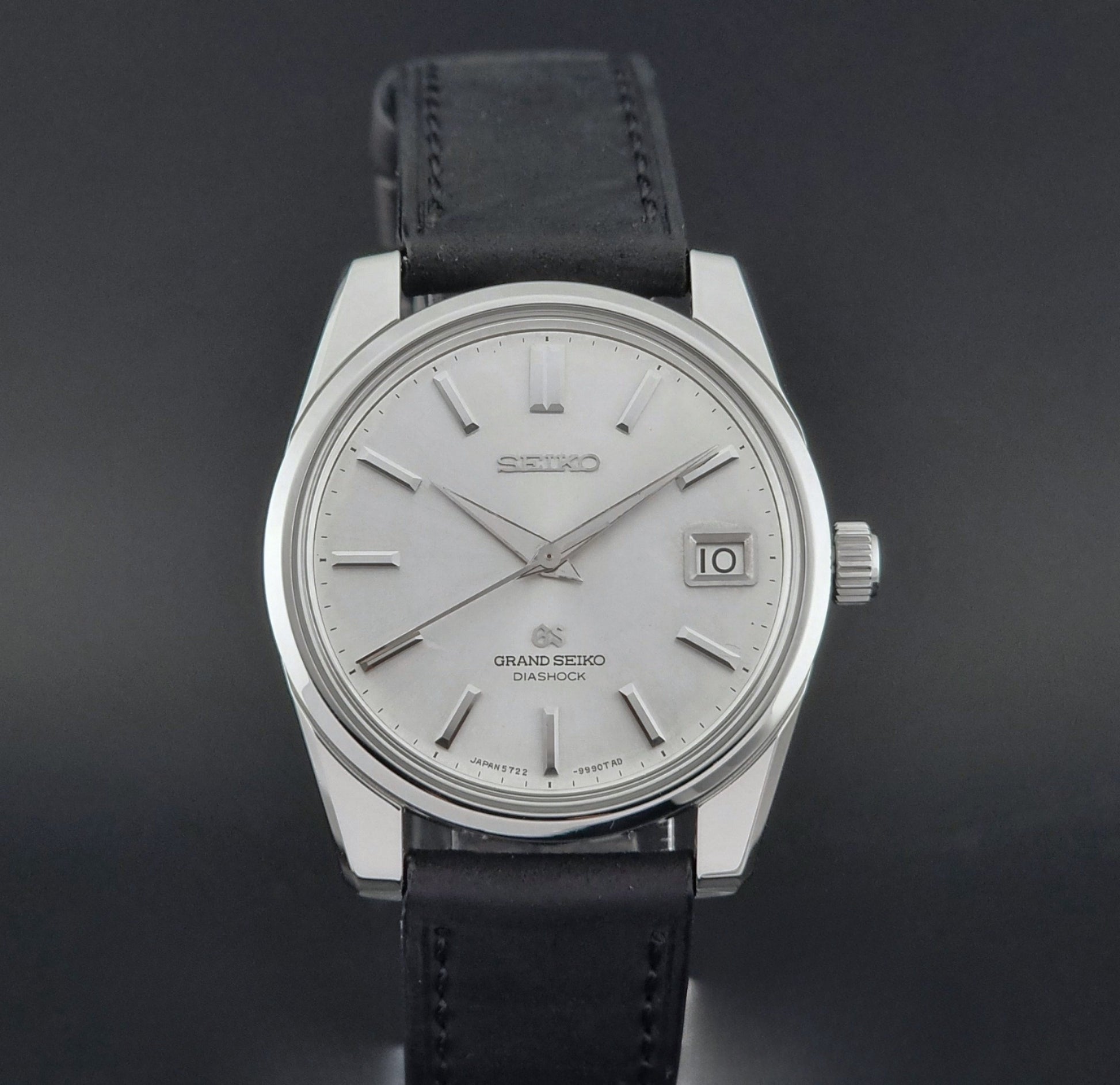 Vintage Grand Seiko Wristwatch 5722-9991 with black leather strap on a gray background front view