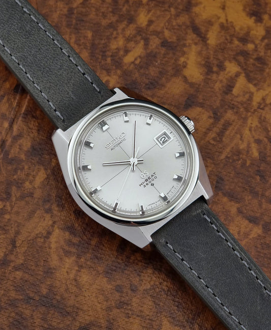 Vintage Grand Seiko watch with silver case and dark leather strap on a wooden surface
