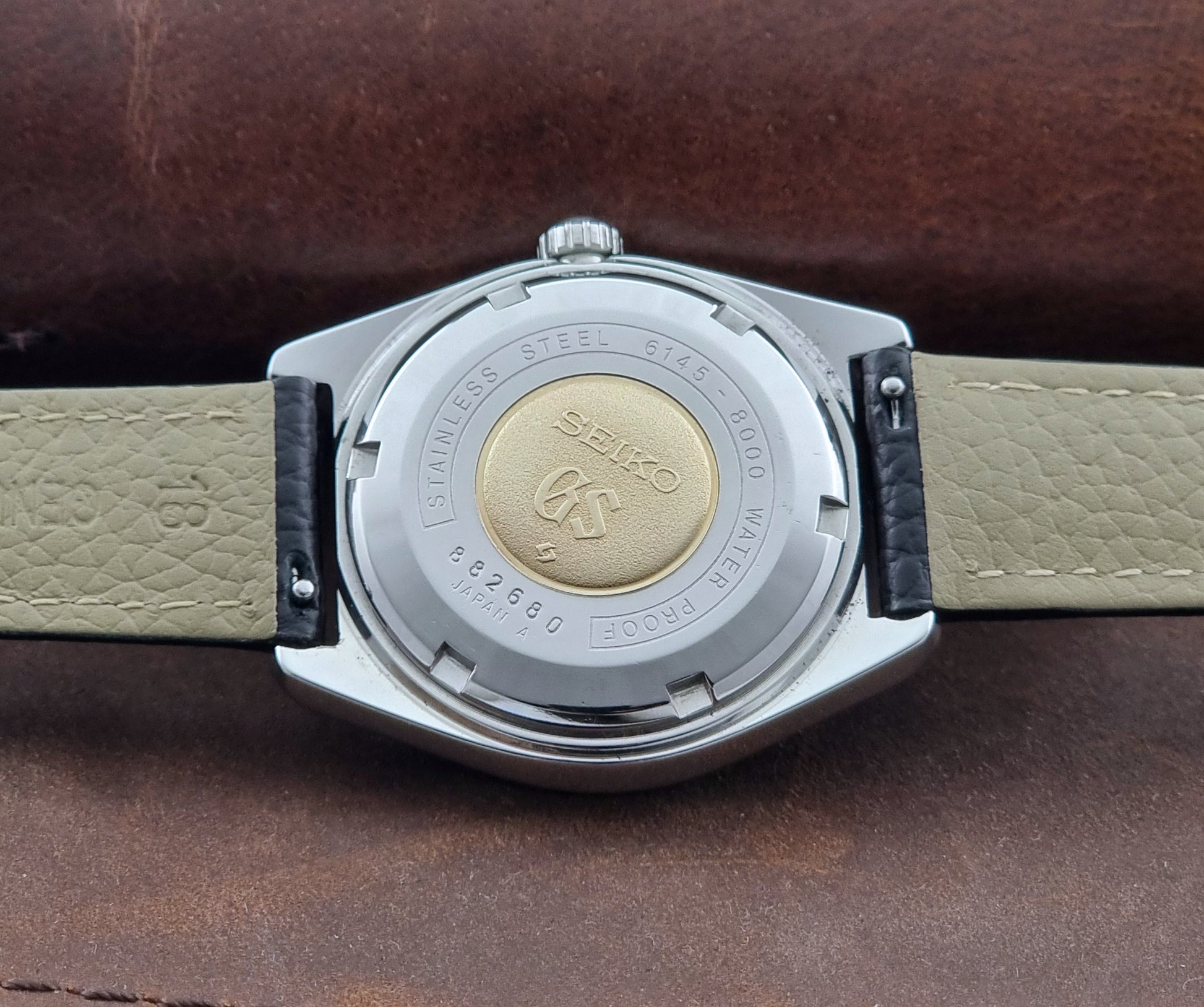 Grand Seiko Wristwatch 6145-8000 with black leather strap on a gray surface case back view