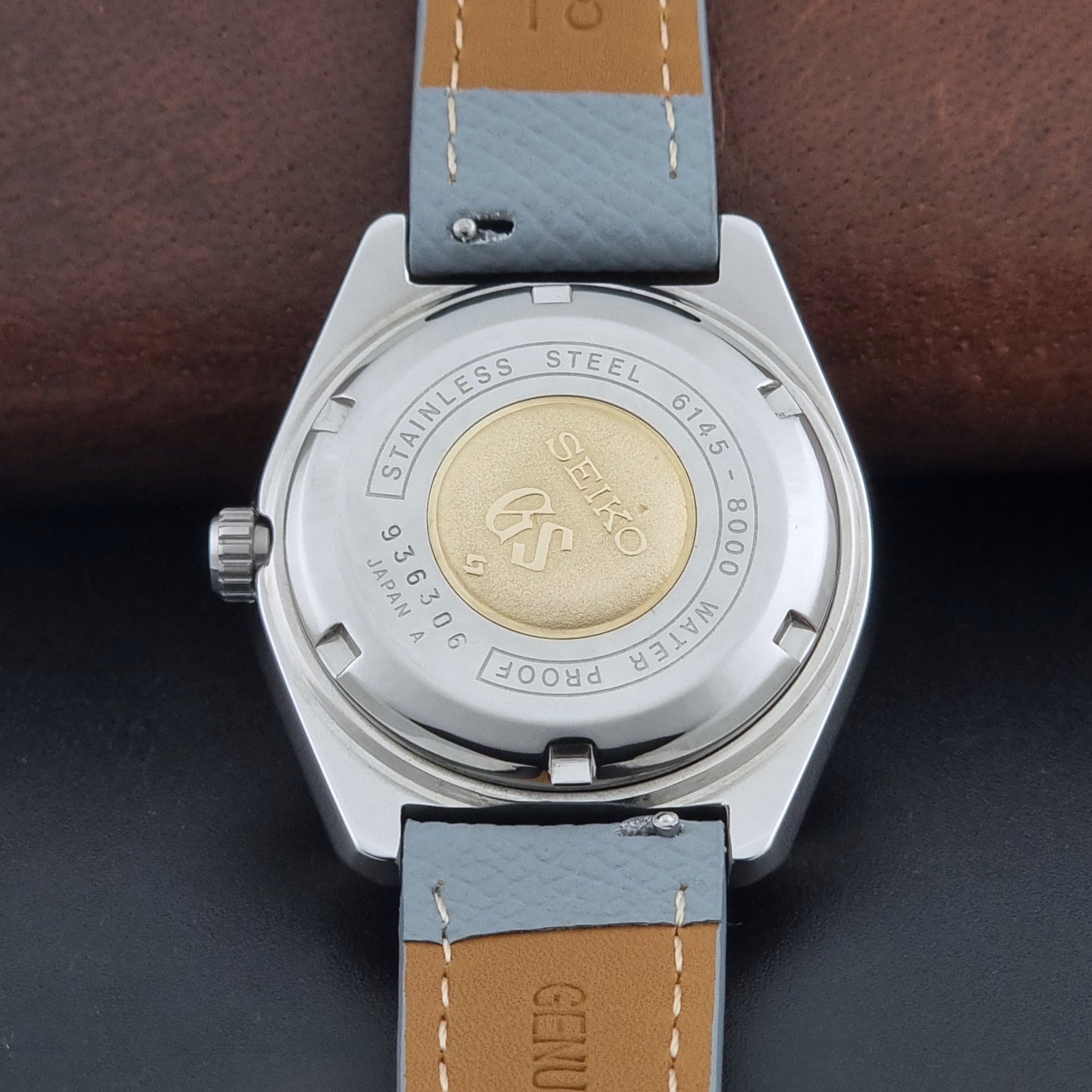 Vintage Grand Seiko 6145-8000 on a grey leather strap on a dark background case back view