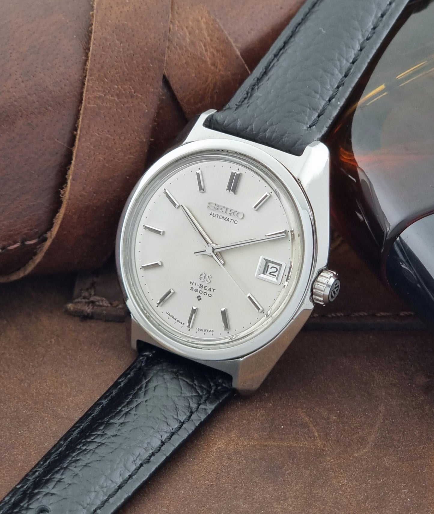 Grand Seiko Wristwatch 6145-8000 with black leather strap on a brown surface crown view