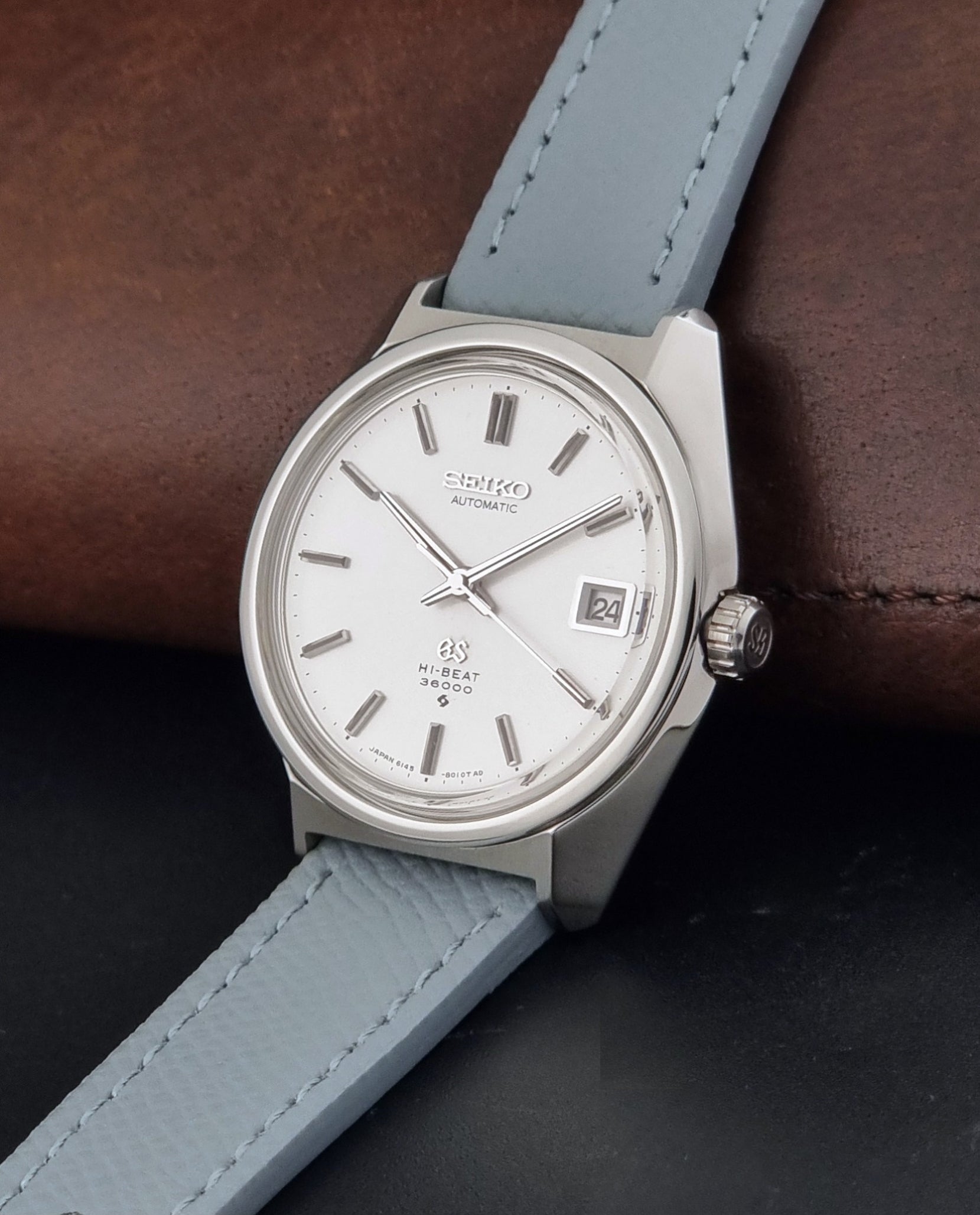 Vintage Grand Seiko 6145-8000 on a grey leather strap on a dark background crown view