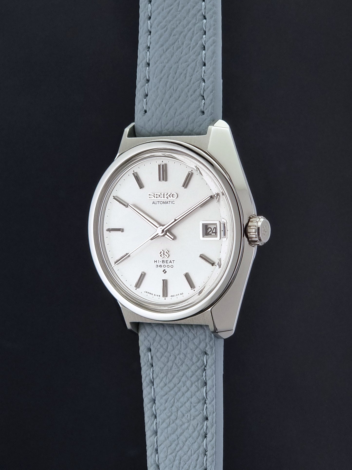 Vintage Grand Seiko 6145-8000 on a grey leather strap on a dark background crown profile view