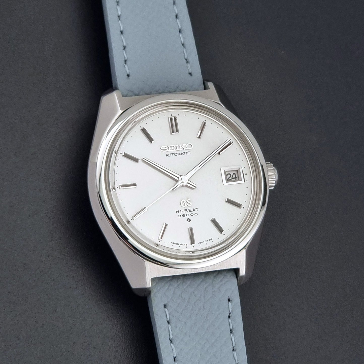 Vintage Grand Seiko 6145-8000 on a grey leather strap on a dark background front view