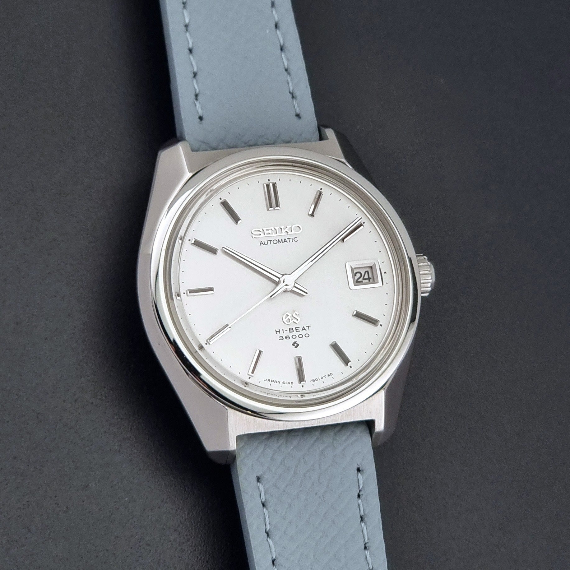 Vintage Grand Seiko 6145-8000 on a grey leather strap on a dark background front view