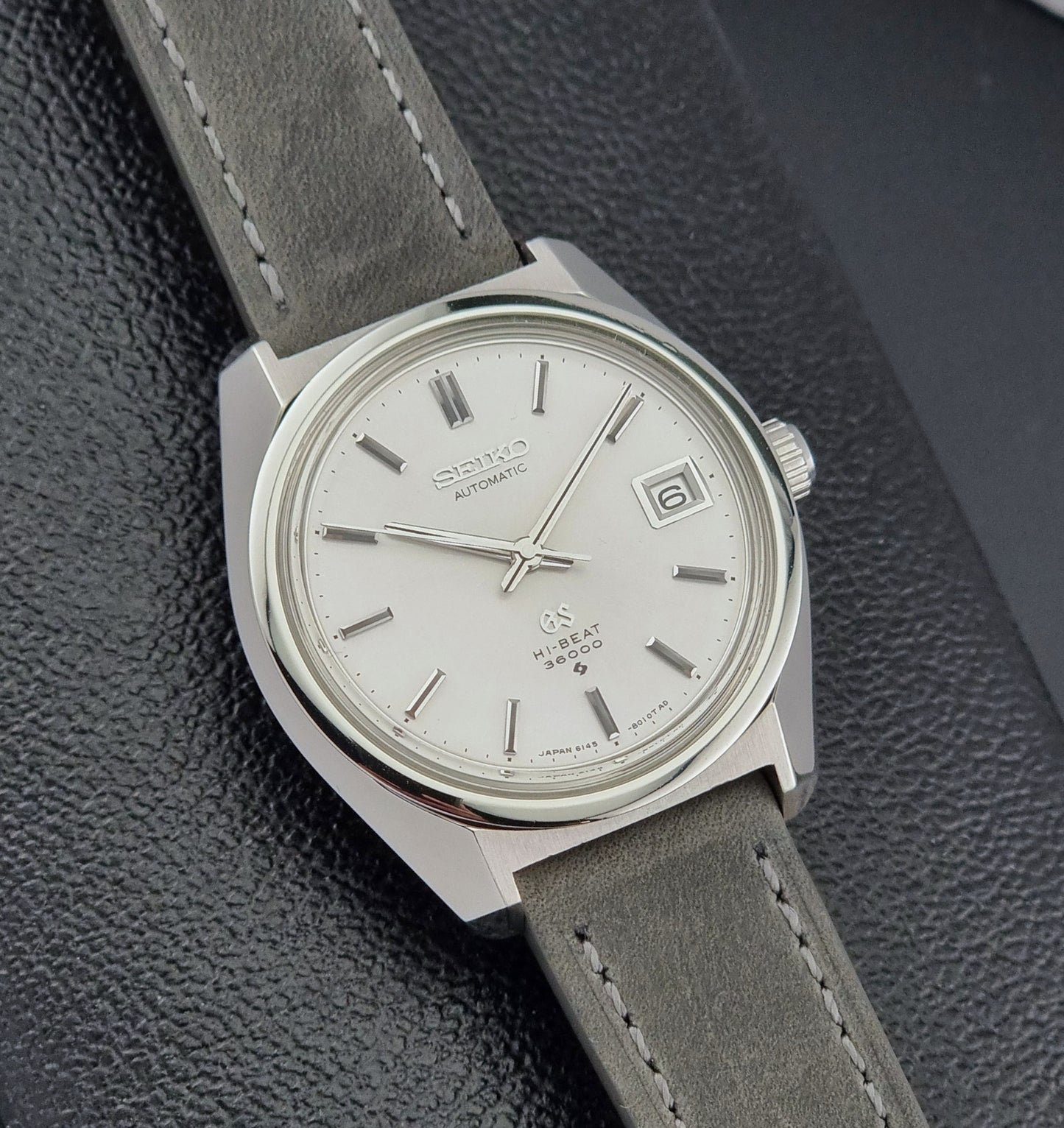 Grand Seiko 6145-8000 Vintage watch with gray leather strap on a textured surface