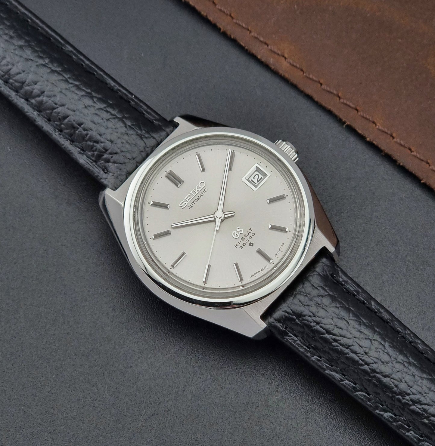 Grand Seiko Wristwatch 6145-8000 with black leather strap on a gray surface front