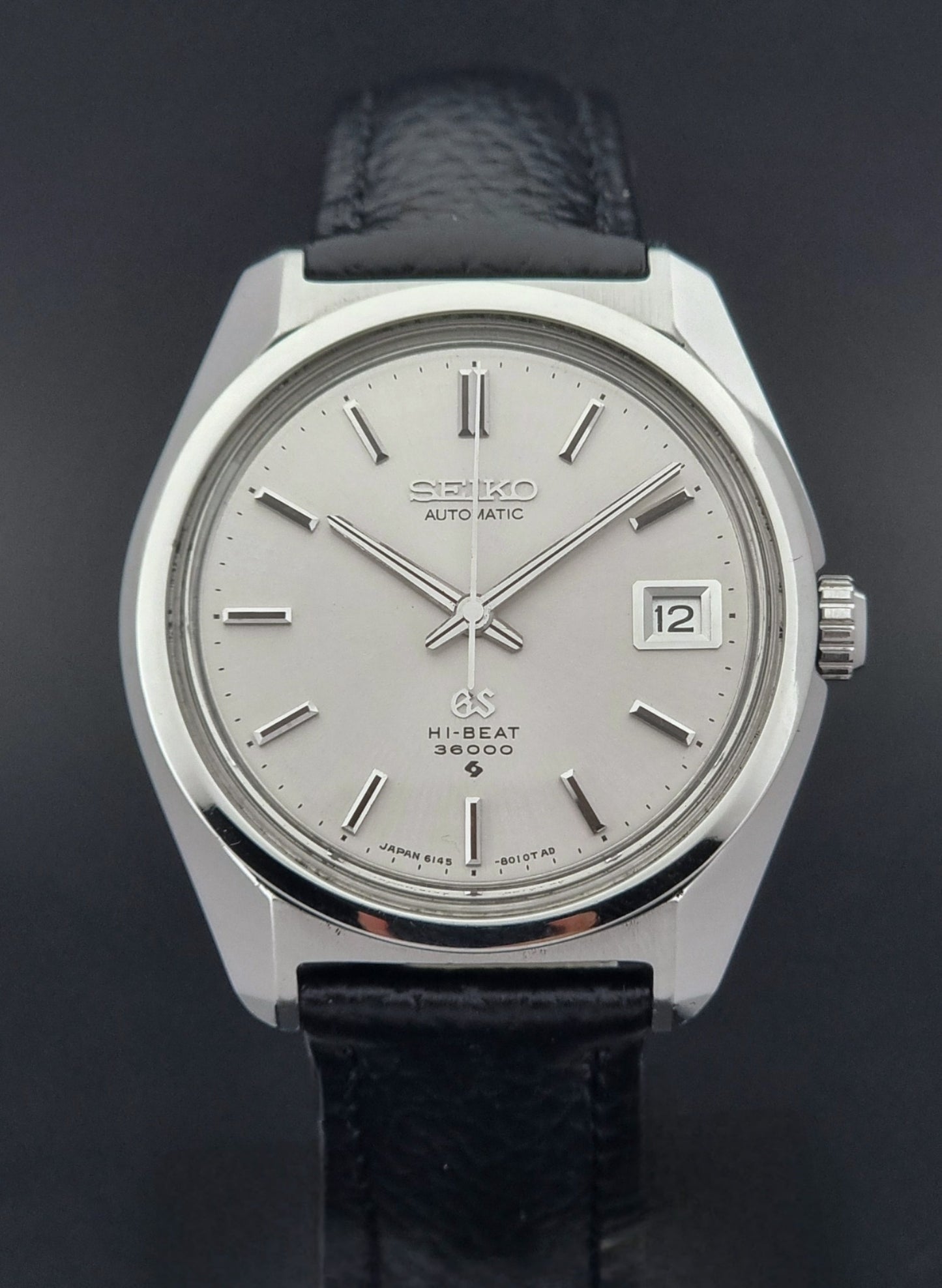 Grand Seiko Wristwatch 6145-8000 with black leather strap on a gray surface dial view