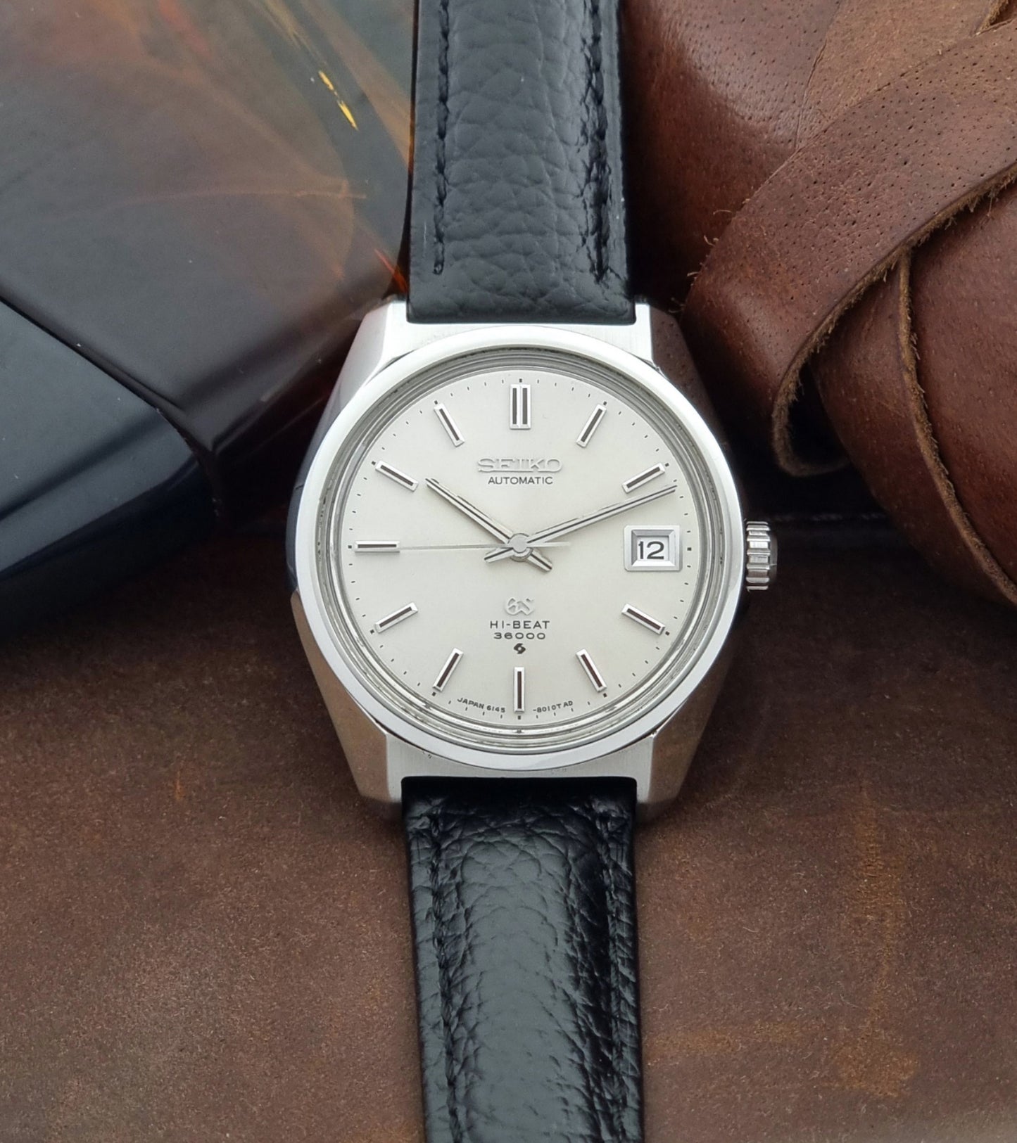 Grand Seiko Wristwatch 6145-8000 with black leather strap on a brown surface front view