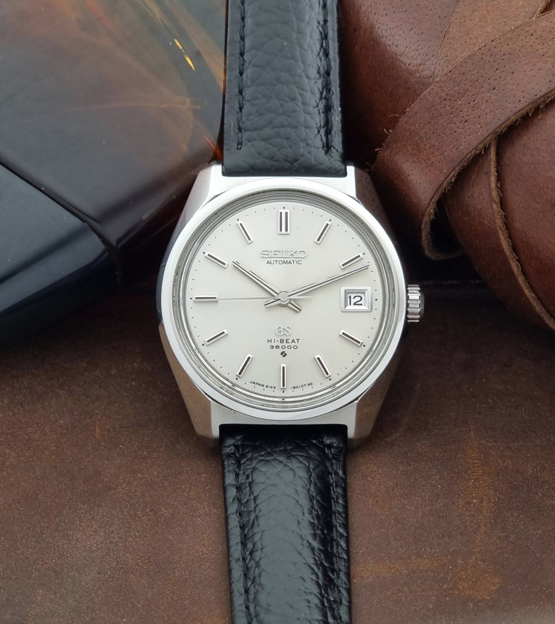 Grand Seiko Wristwatch 6145-8000 with black leather strap on a brown surface front view