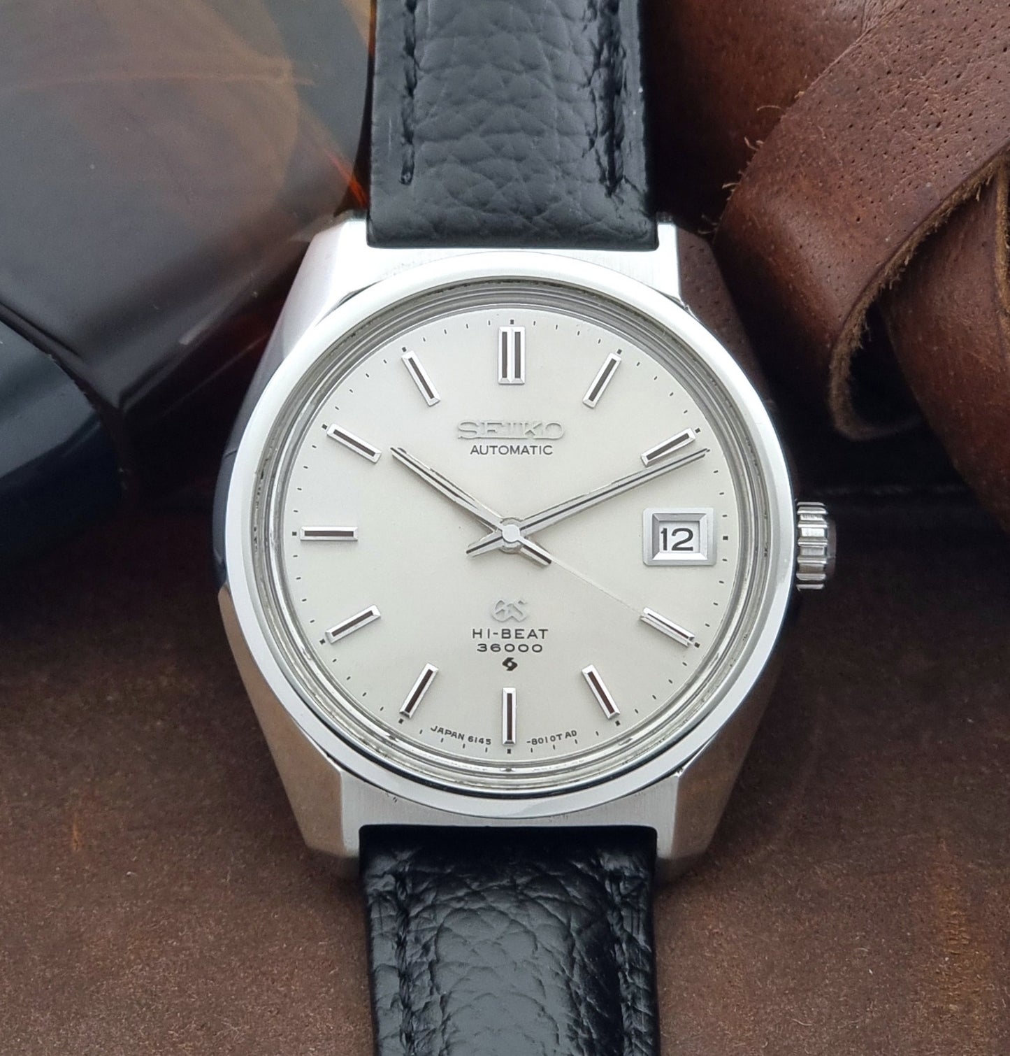 Grand Seiko Wristwatch 6145-8000 with black leather strap on a brown surface close up dial view