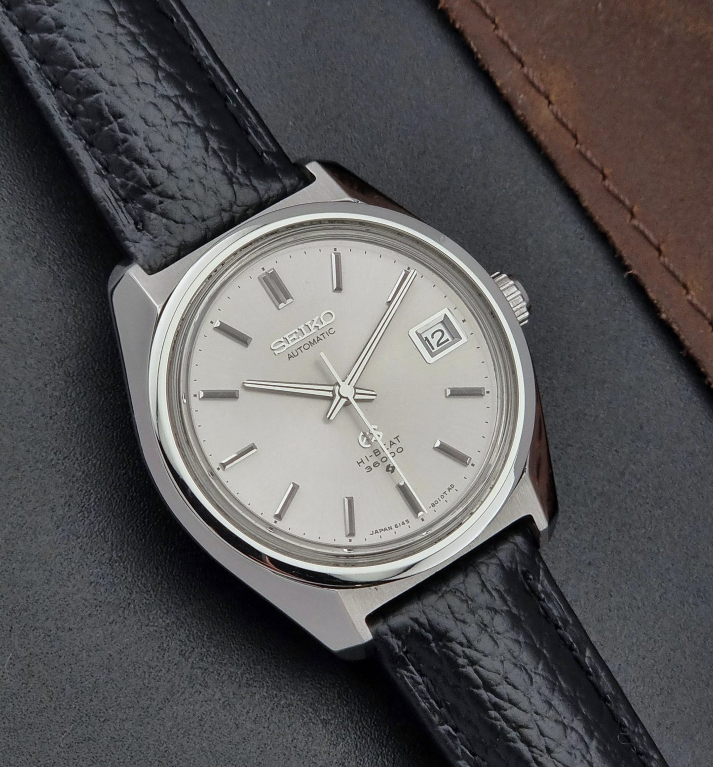 Grand Seiko Wristwatch 6145-8000 with black leather strap on a gray surface close dial view